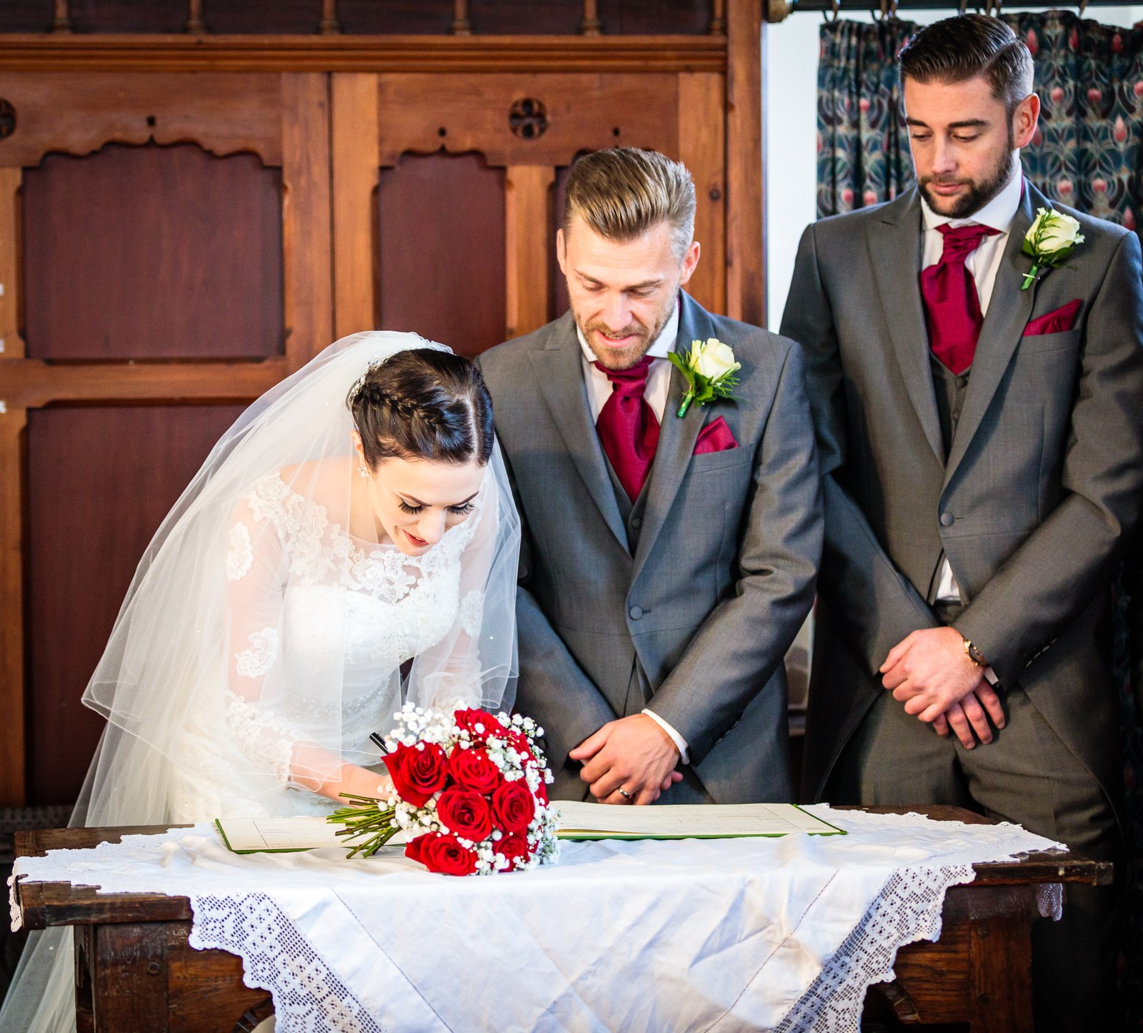 Bride and groom sign the register with a groomsman looking on