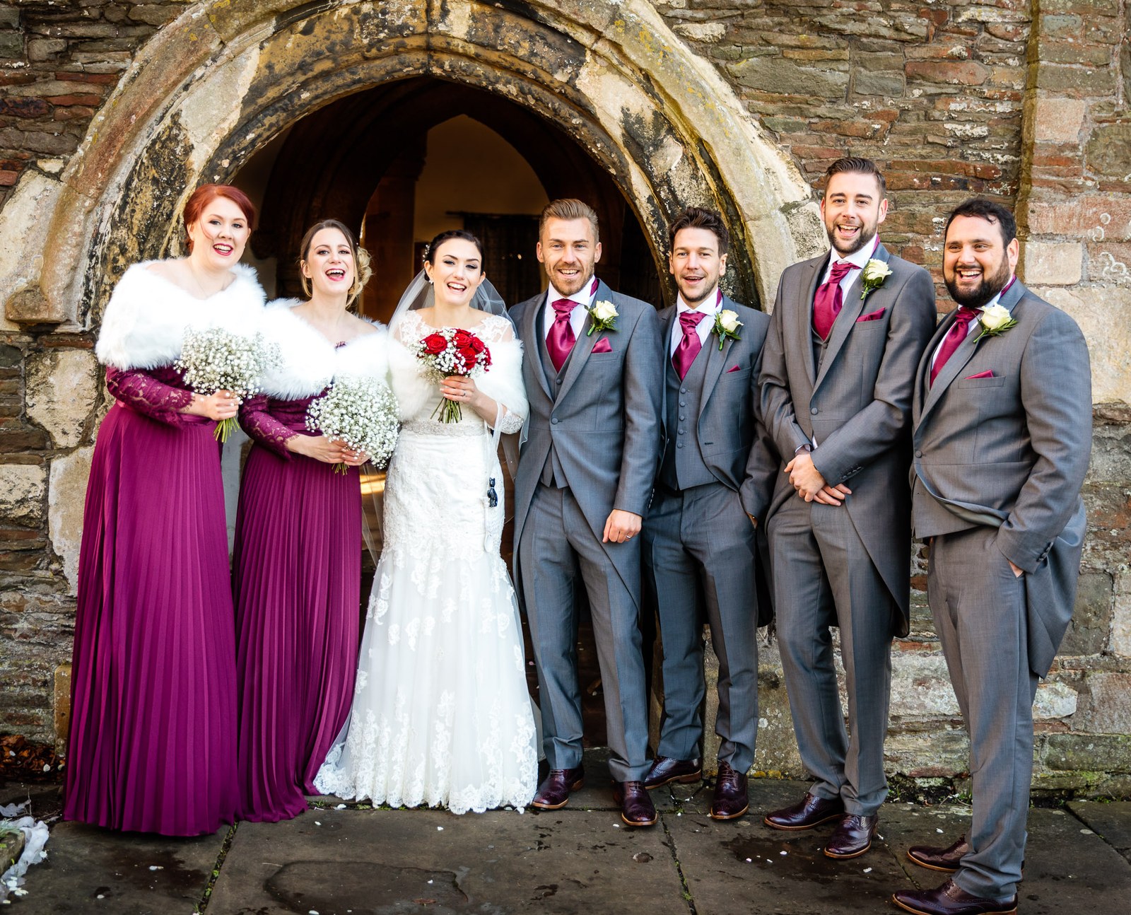 The full wedding party framed in the church's medieval stone arch