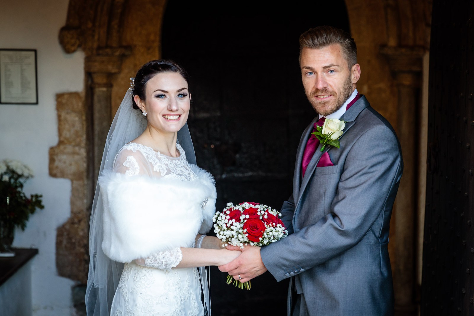The couple pause together in the shadowed church porch