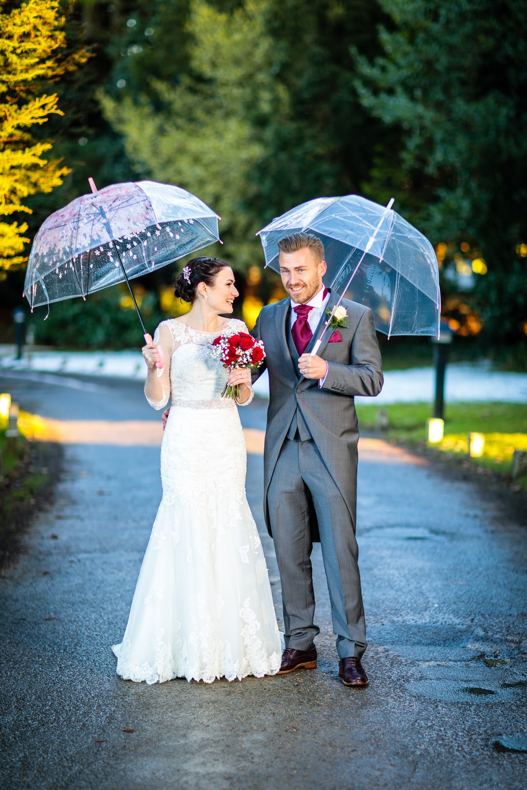 The couple share clear umbrellas along the tree-lined approach
