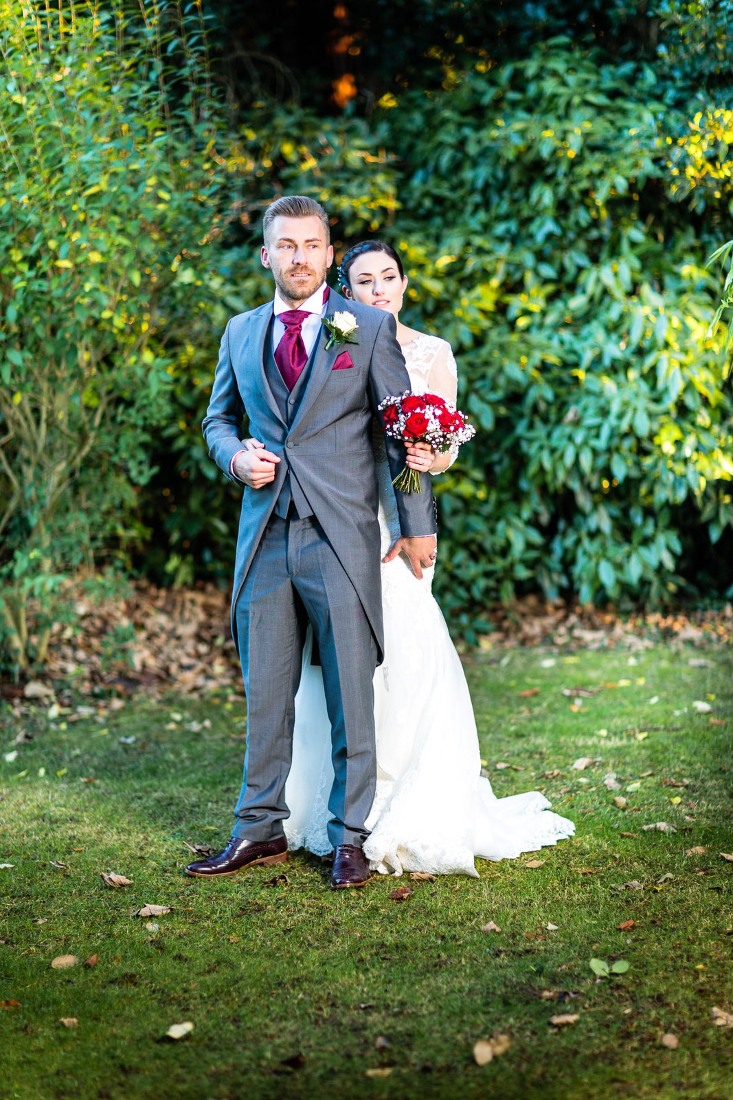 The bride holds her bouquet as she nestles behind the groom in the garden