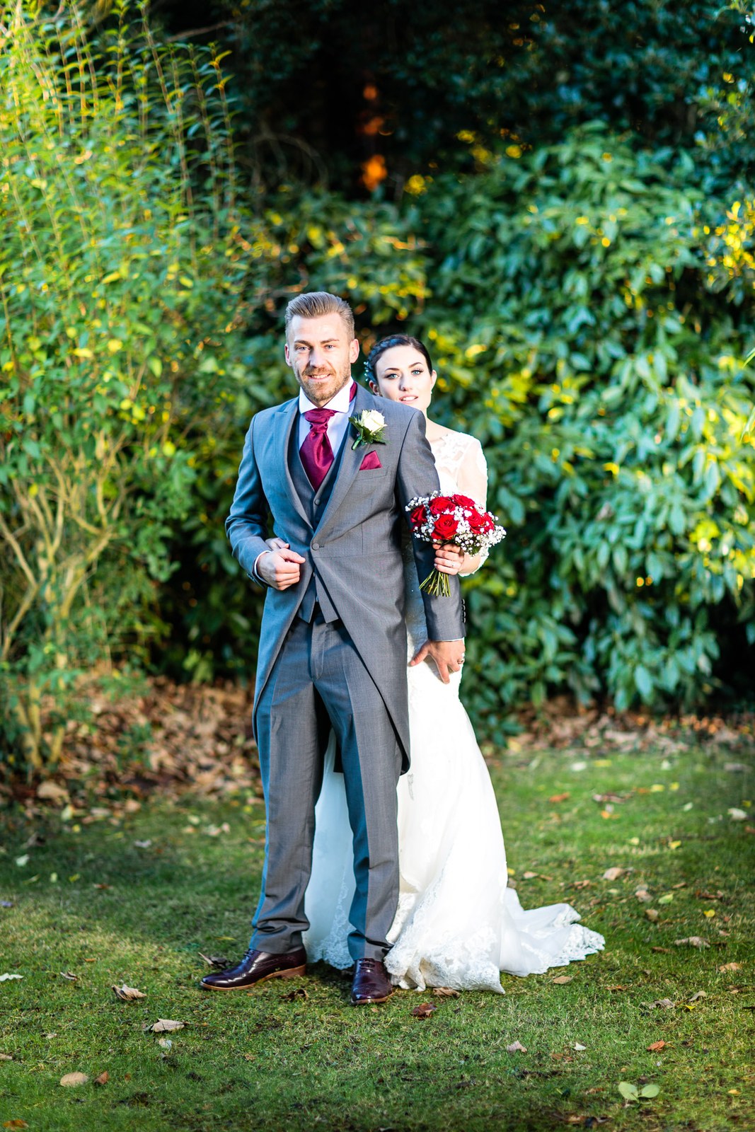 Bride and groom together among the evergreen shrubs of the grounds