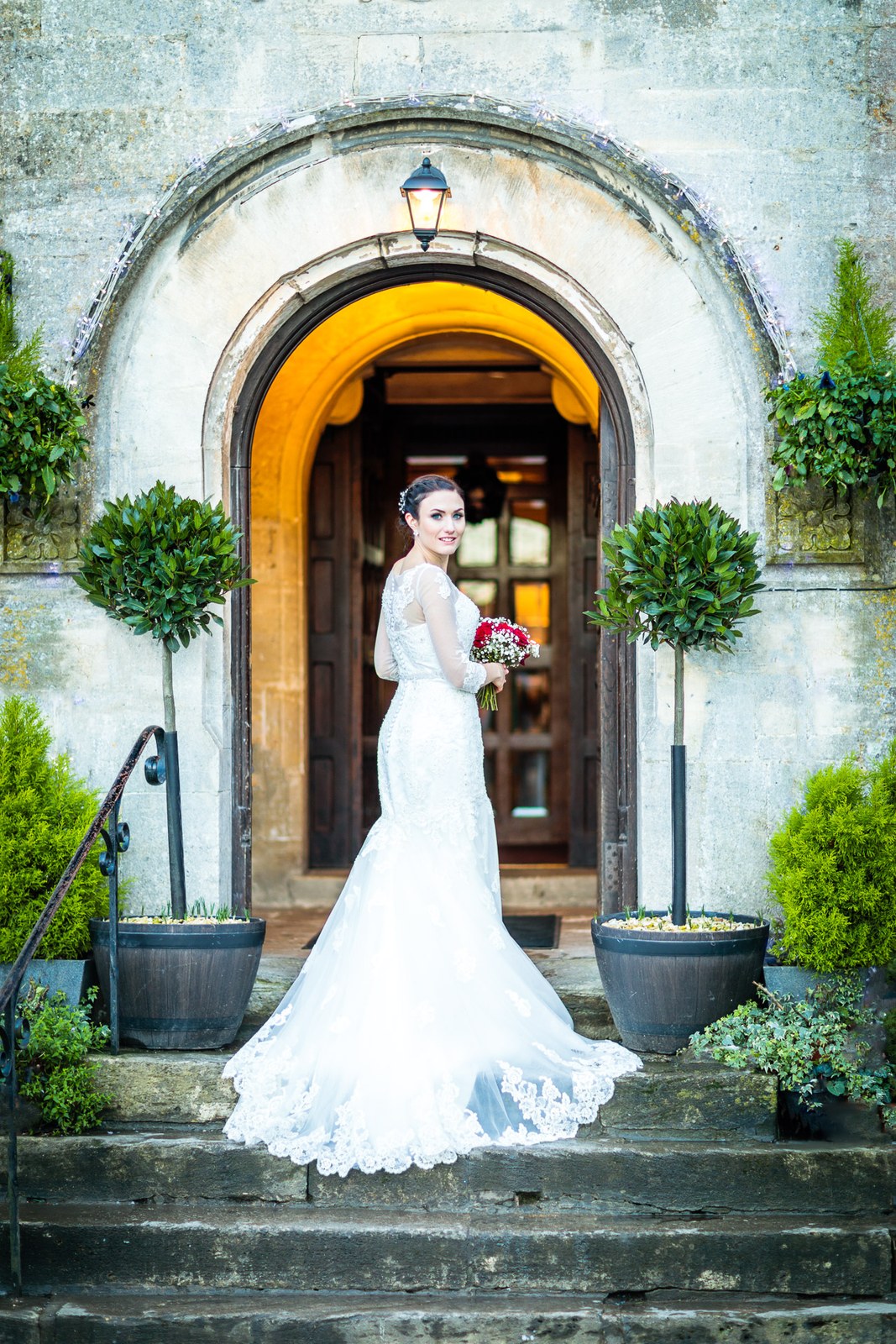 Bride poses in the arched stone entrance of Stonehouse Court Hotel, dress trailing the steps