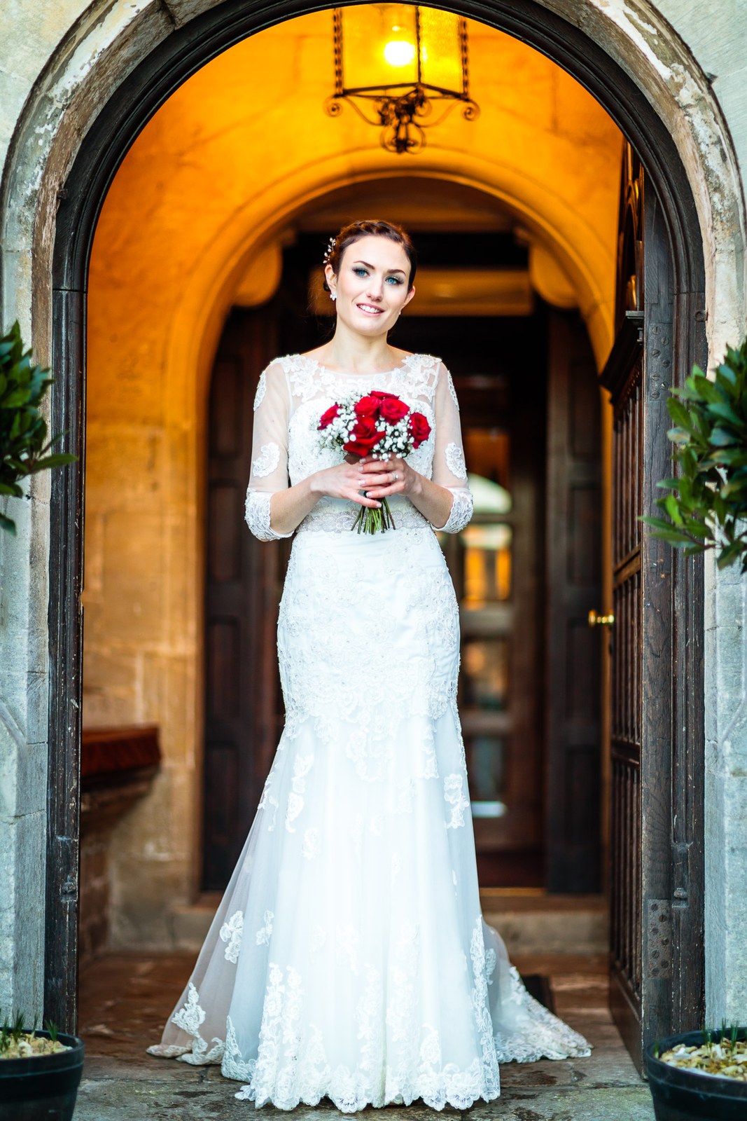 Bride holds her bouquet framed in the lamp-lit doorway of Stonehouse Court Hotel