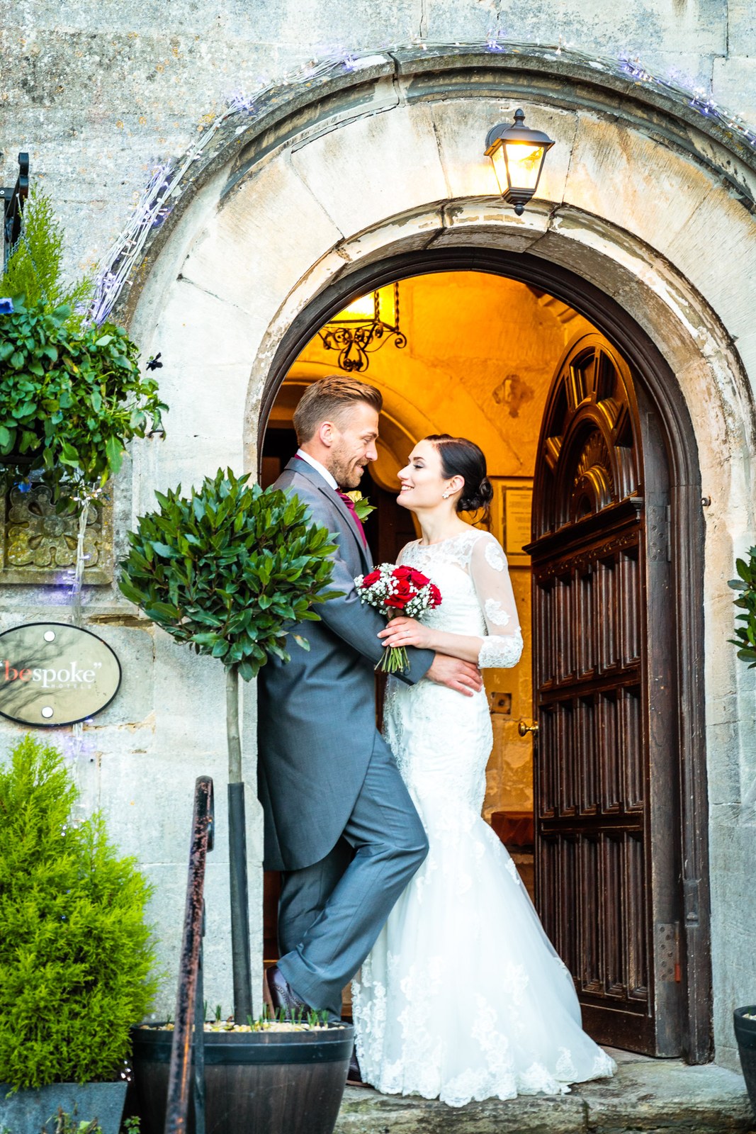 The groom leans in the stone archway of Stonehouse Court Hotel beside his bride