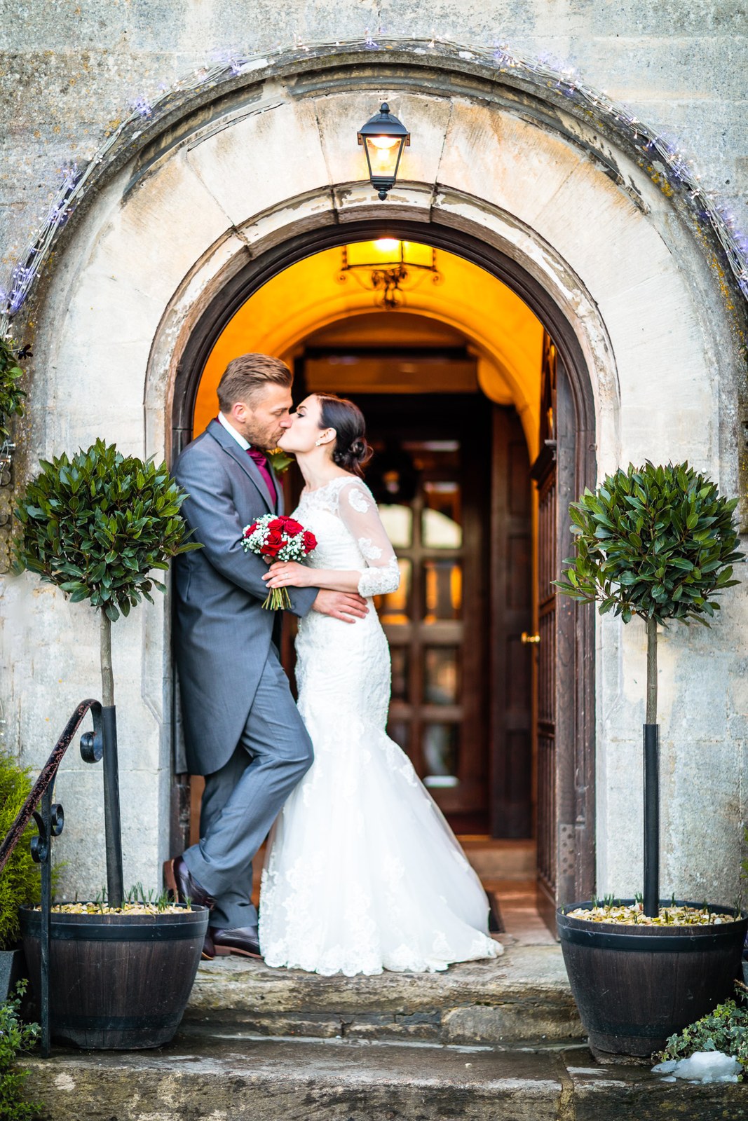 Bride and groom kiss in the glowing arched entrance of Stonehouse Court Hotel