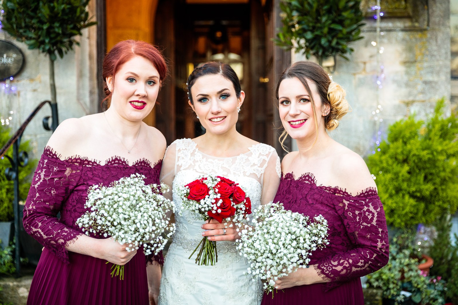 Bride flanked by two bridesmaids holding gypsophila and red rose bouquets