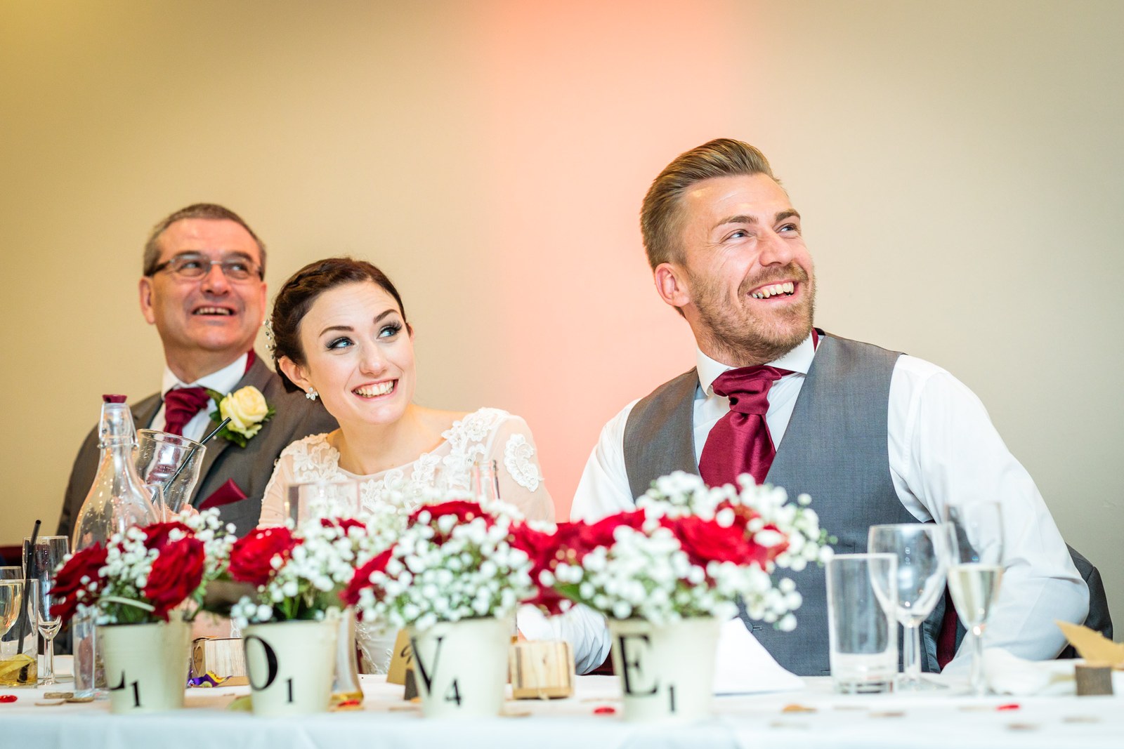 Bride laughs between her father and groom at the flower-dressed top table