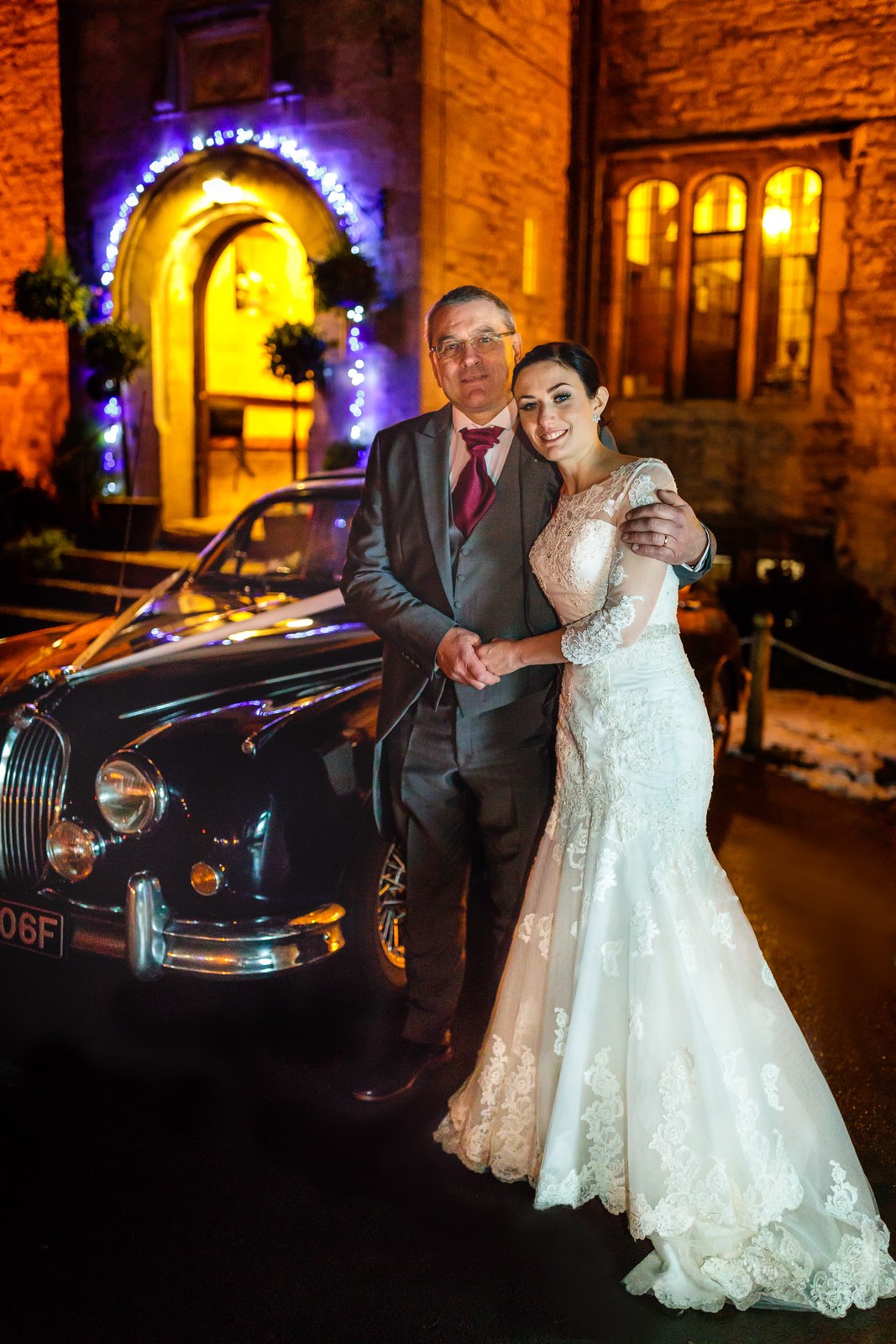 Bride and her father beside the vintage Jaguar before the floodlit Stonehouse Court Hotel