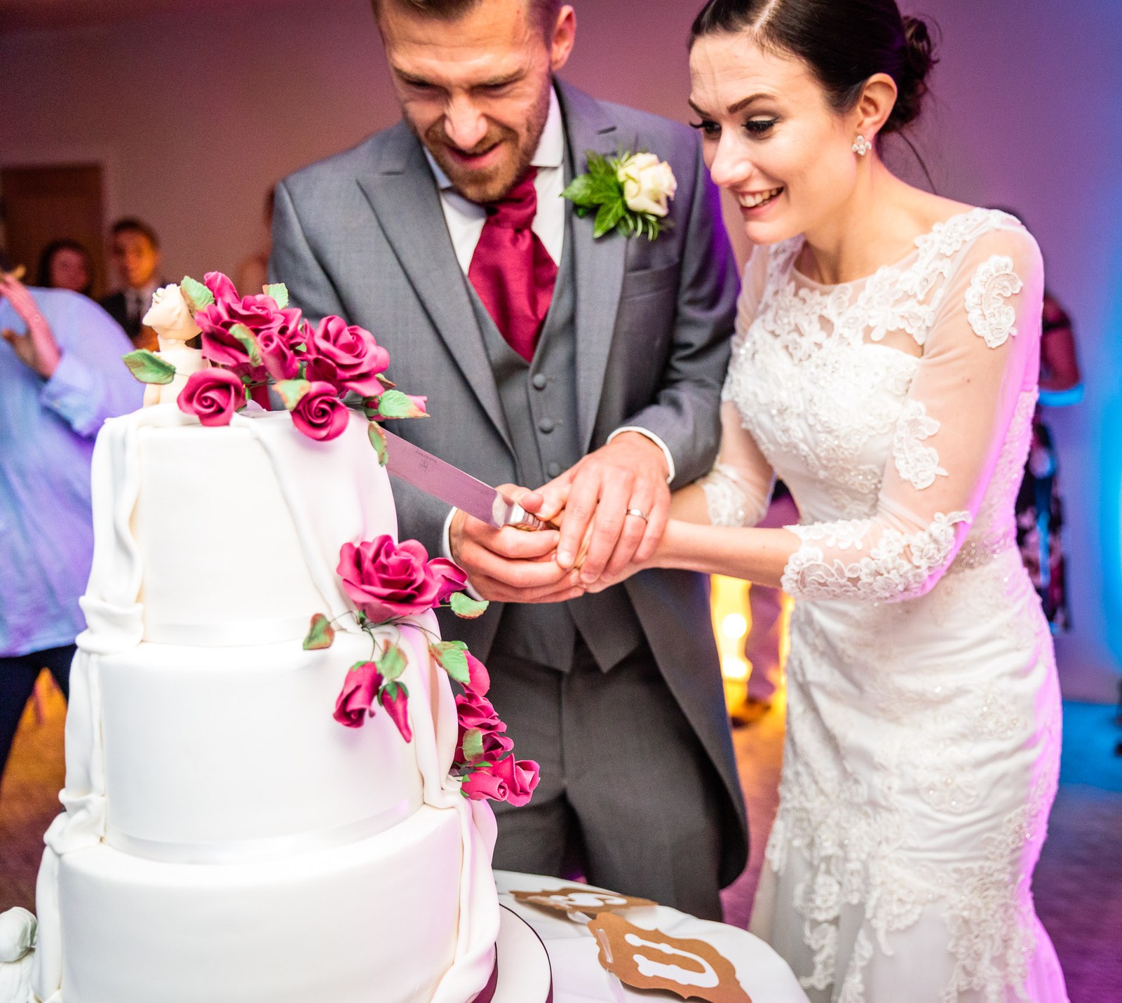 Bride and groom cut their tall white cake dressed with pink roses