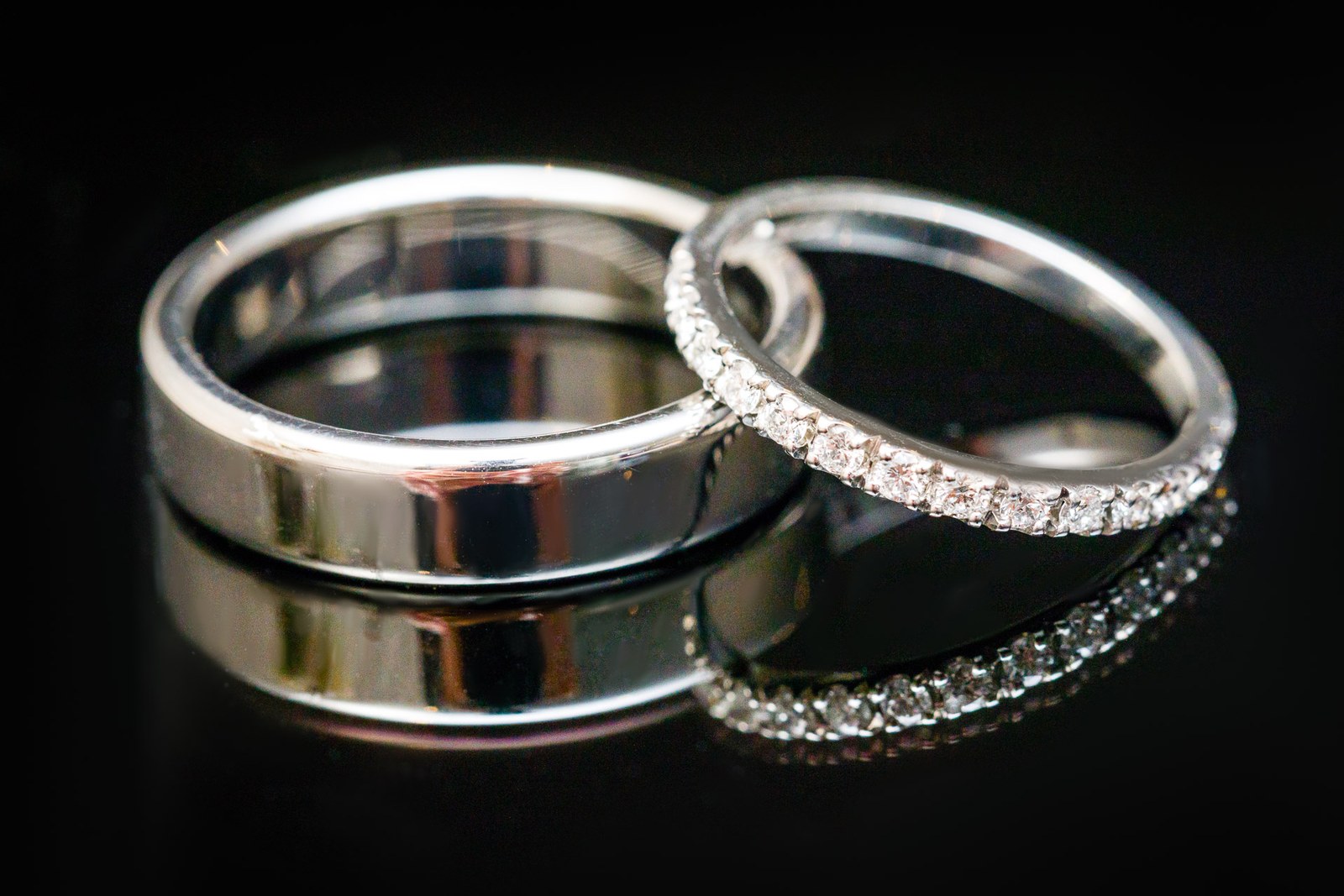 A diamond band nested beside a plain wedding ring on dark glass