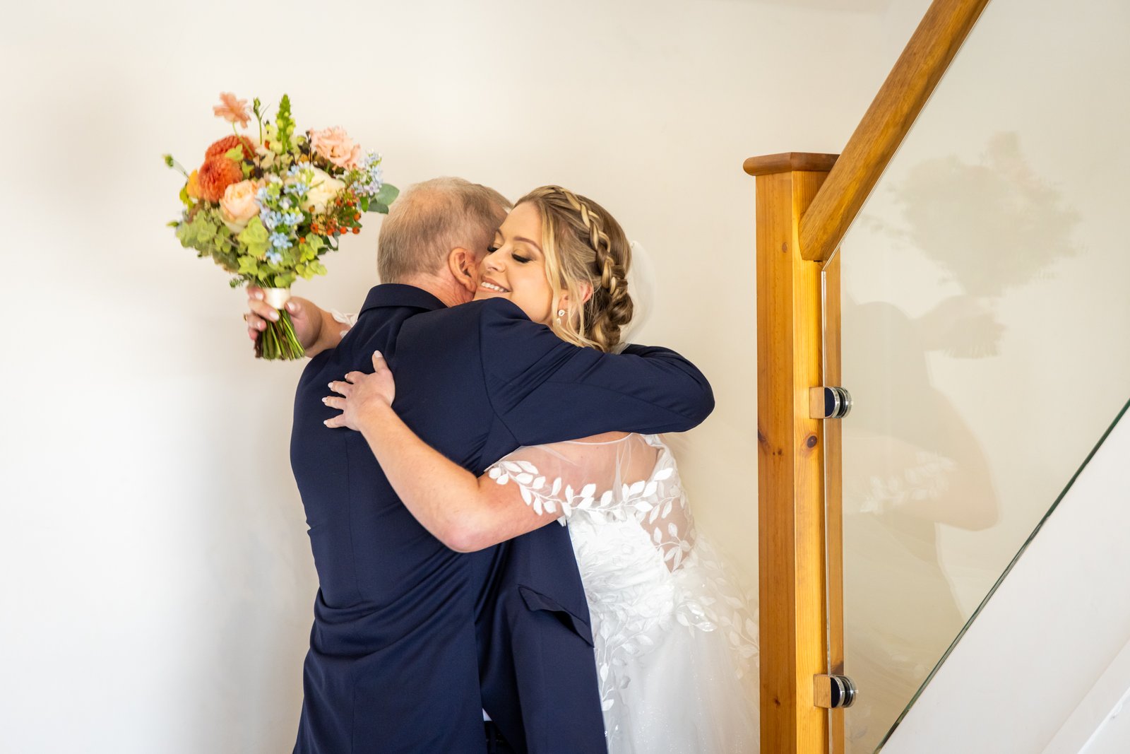 The bride embracing a suited guest who is holding her bouquet behind her shoulder.