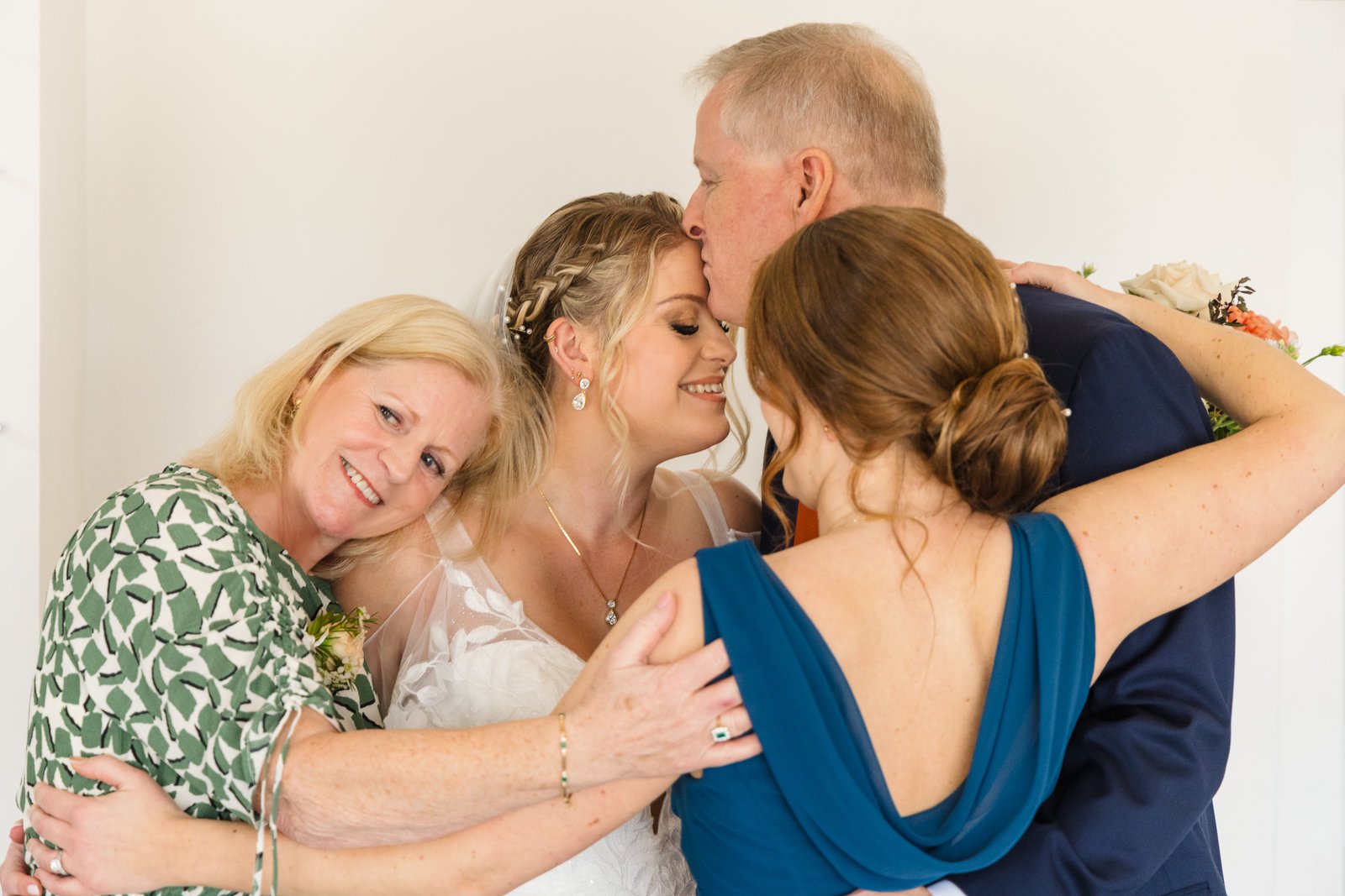 The bride in a group hug with guests, one of them kissing the top of her head.
