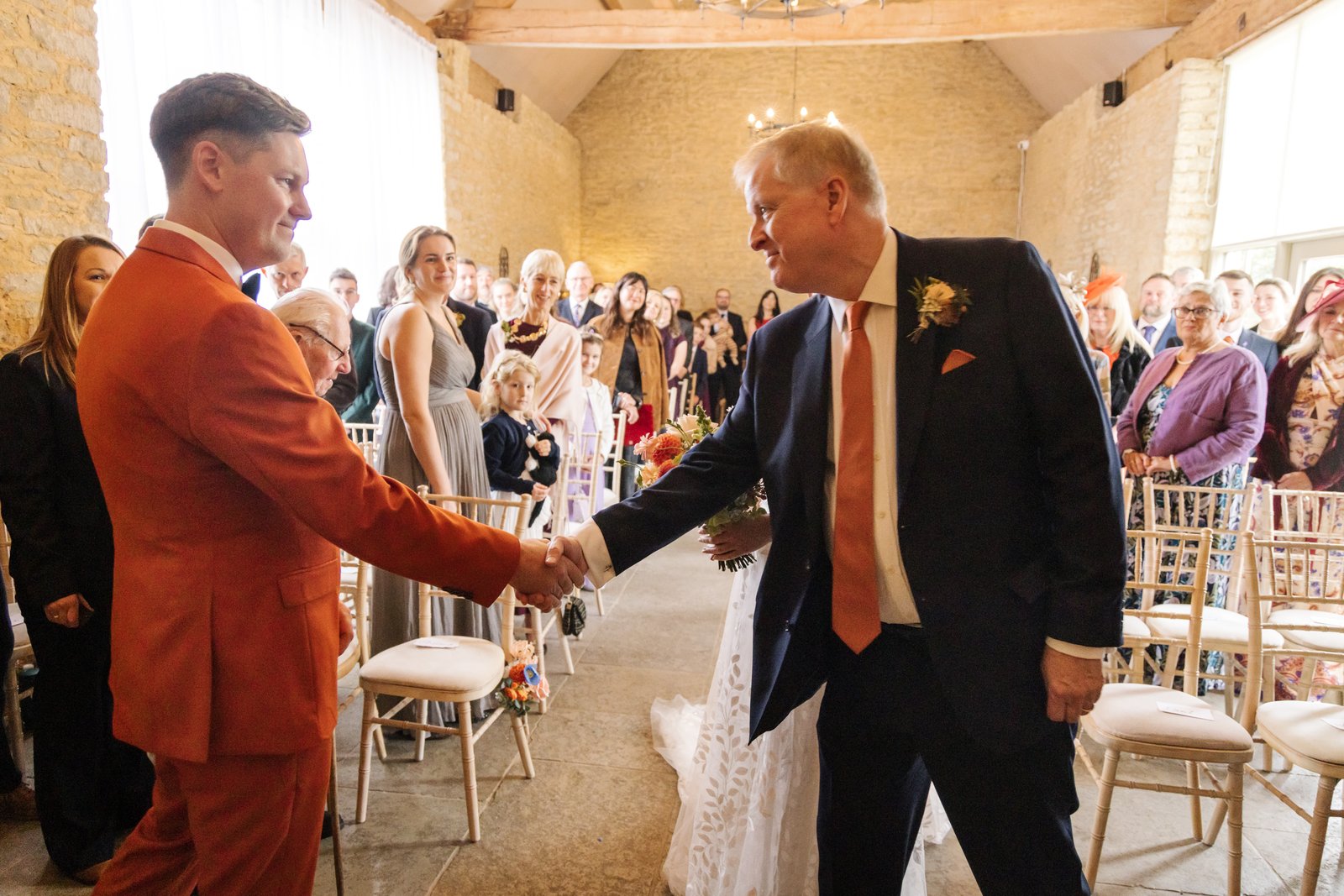 The groom shaking hands with the bride's father at the top of the aisle.