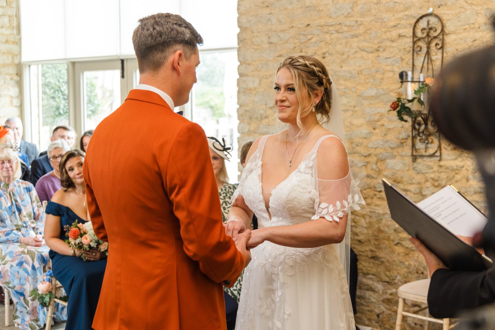 The couple holding hands during the ceremony, the tall windows of Stratton Court Barn behind.