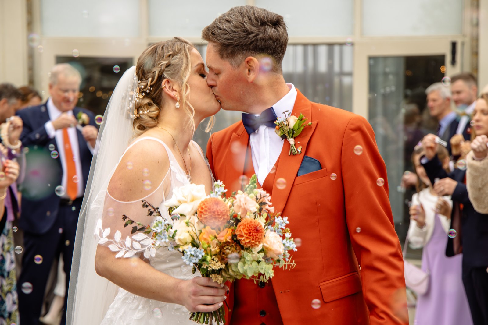 The couple kissing in a cloud of bubbles as guests blow them from both sides.