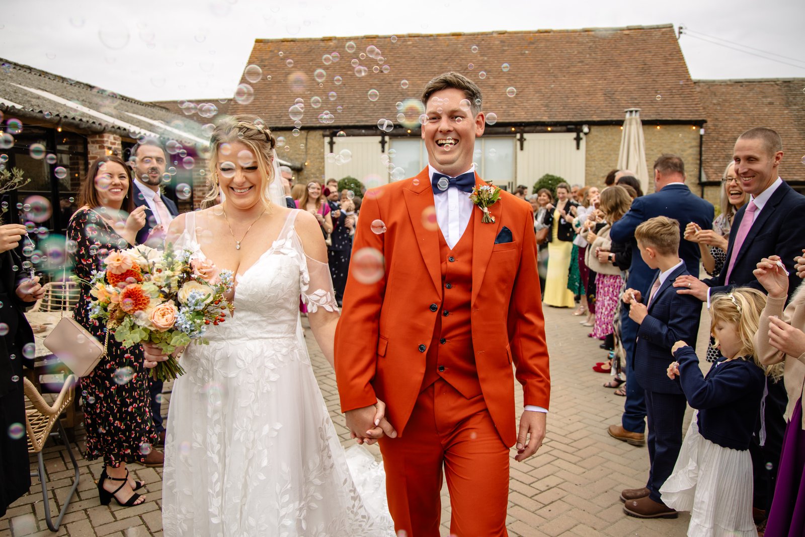 The bride and groom walking out through bubbles into the courtyard at Stratton Court Barn.