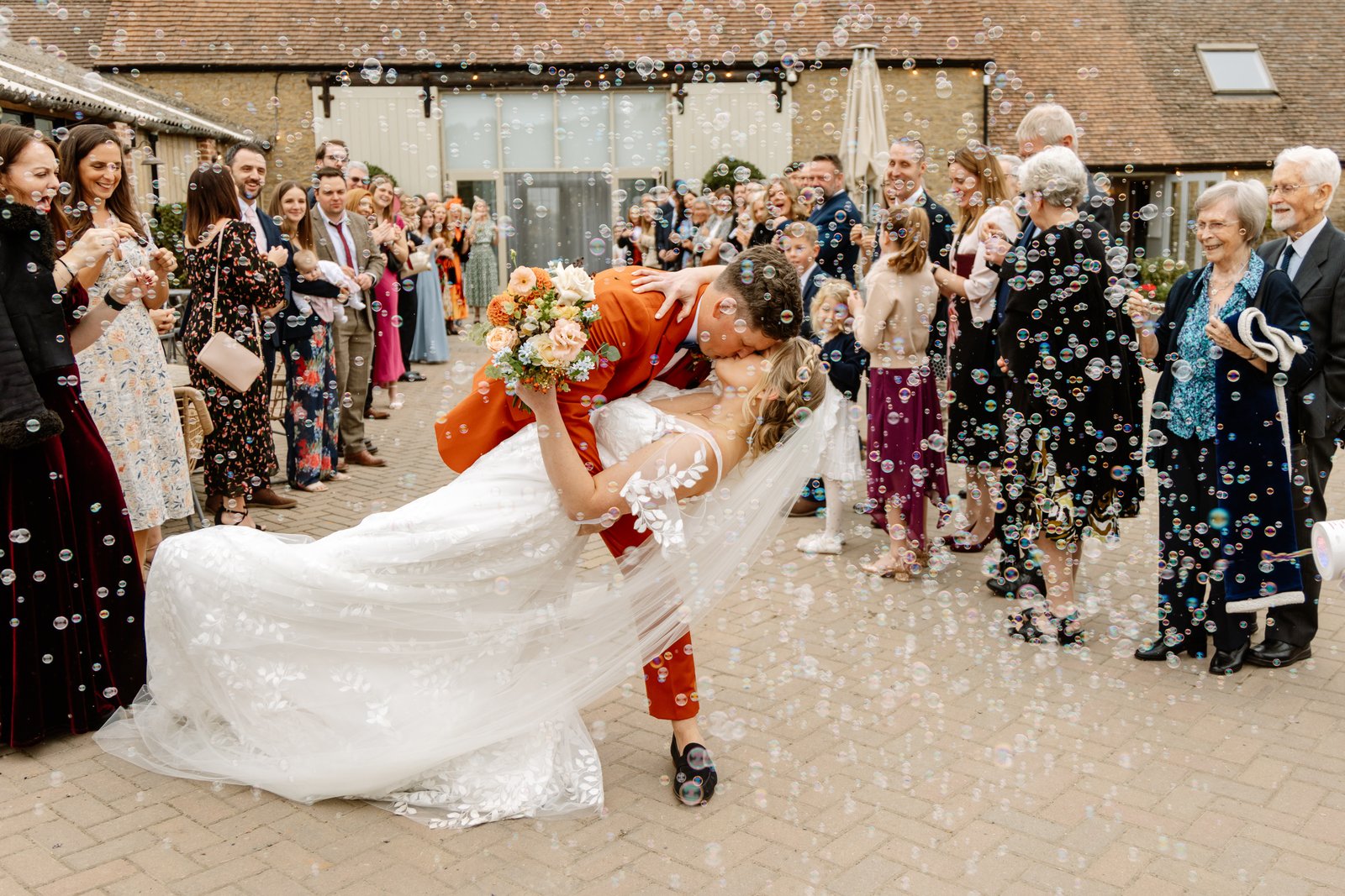 The groom dipping the bride for a kiss as guests throw confetti in the courtyard.