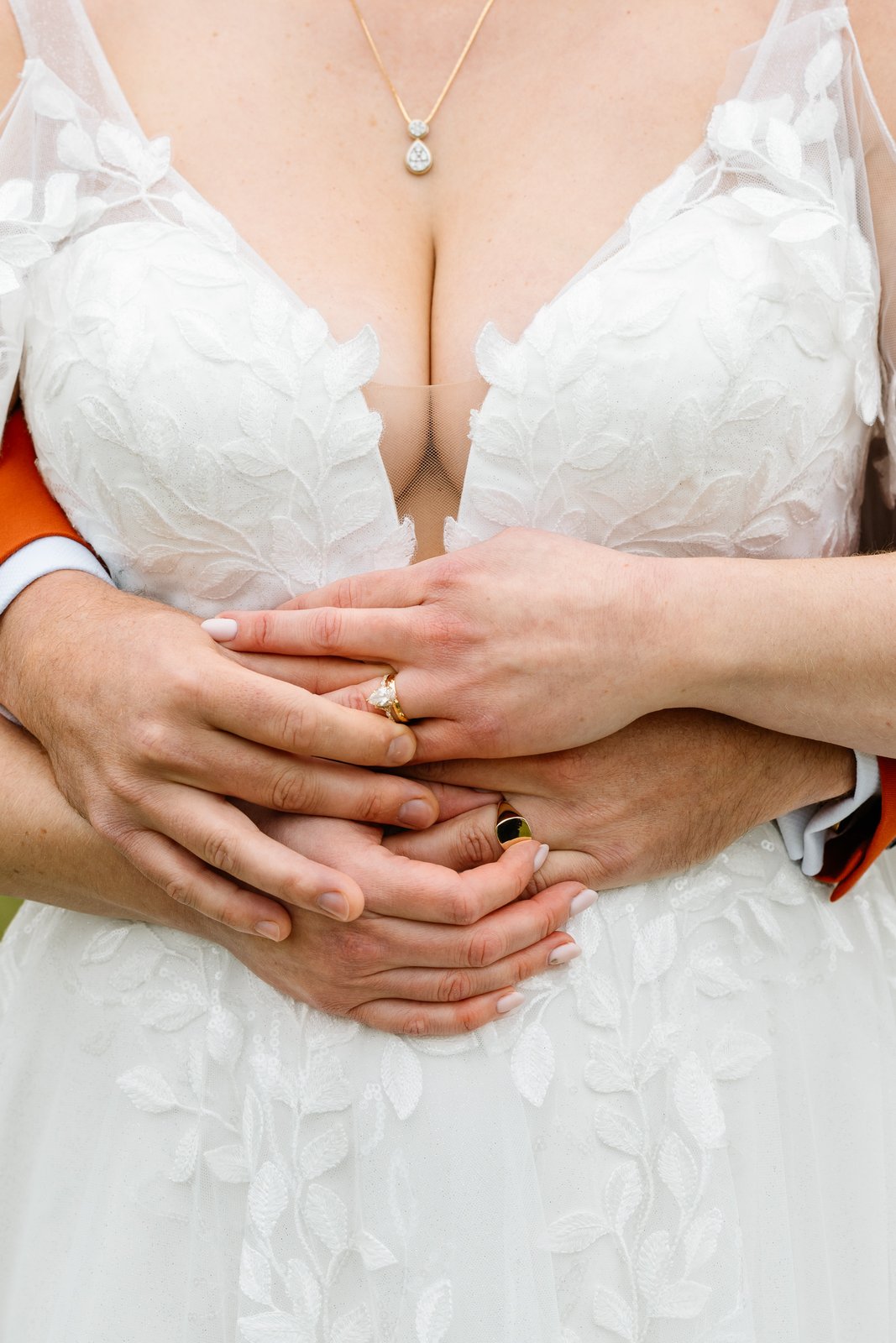 The bride's hands resting over the lace bodice of her gown, wedding ring showing.