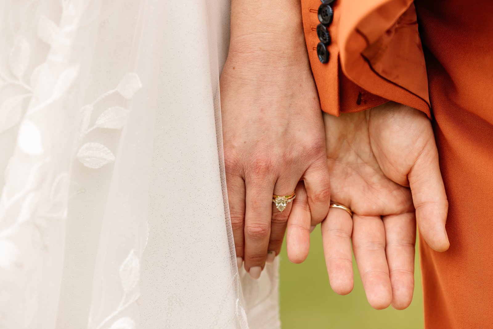 The couple's hands side by side, both wedding rings against the lace of the dress.