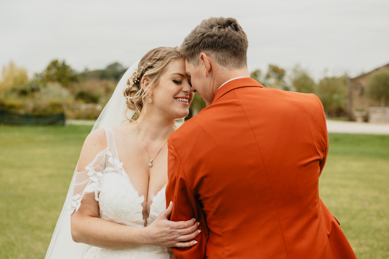 The bride and groom close together on the grass, an autumn hedgerow behind them.