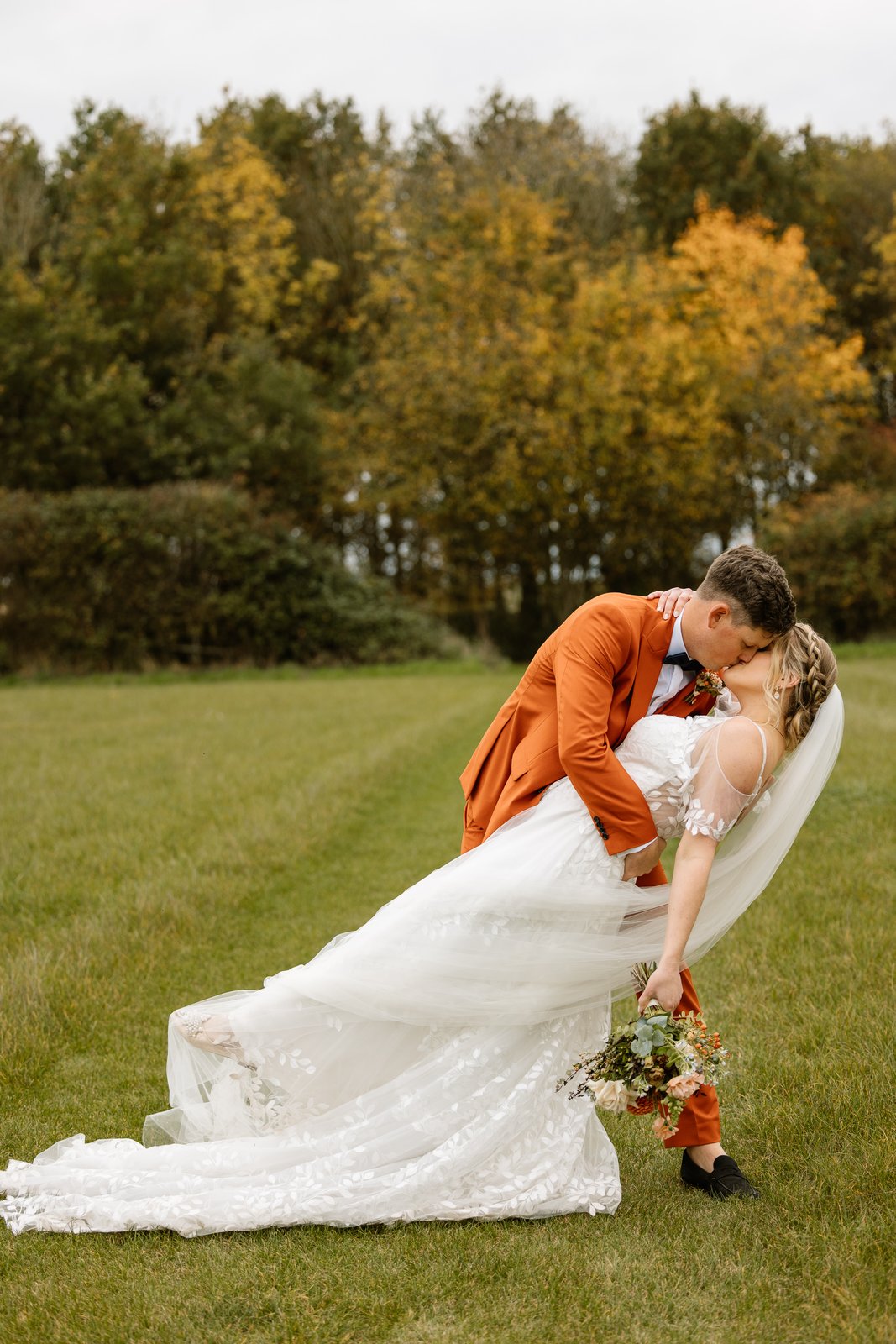 The groom leaning the bride back for a kiss, her train spread out on the grass.