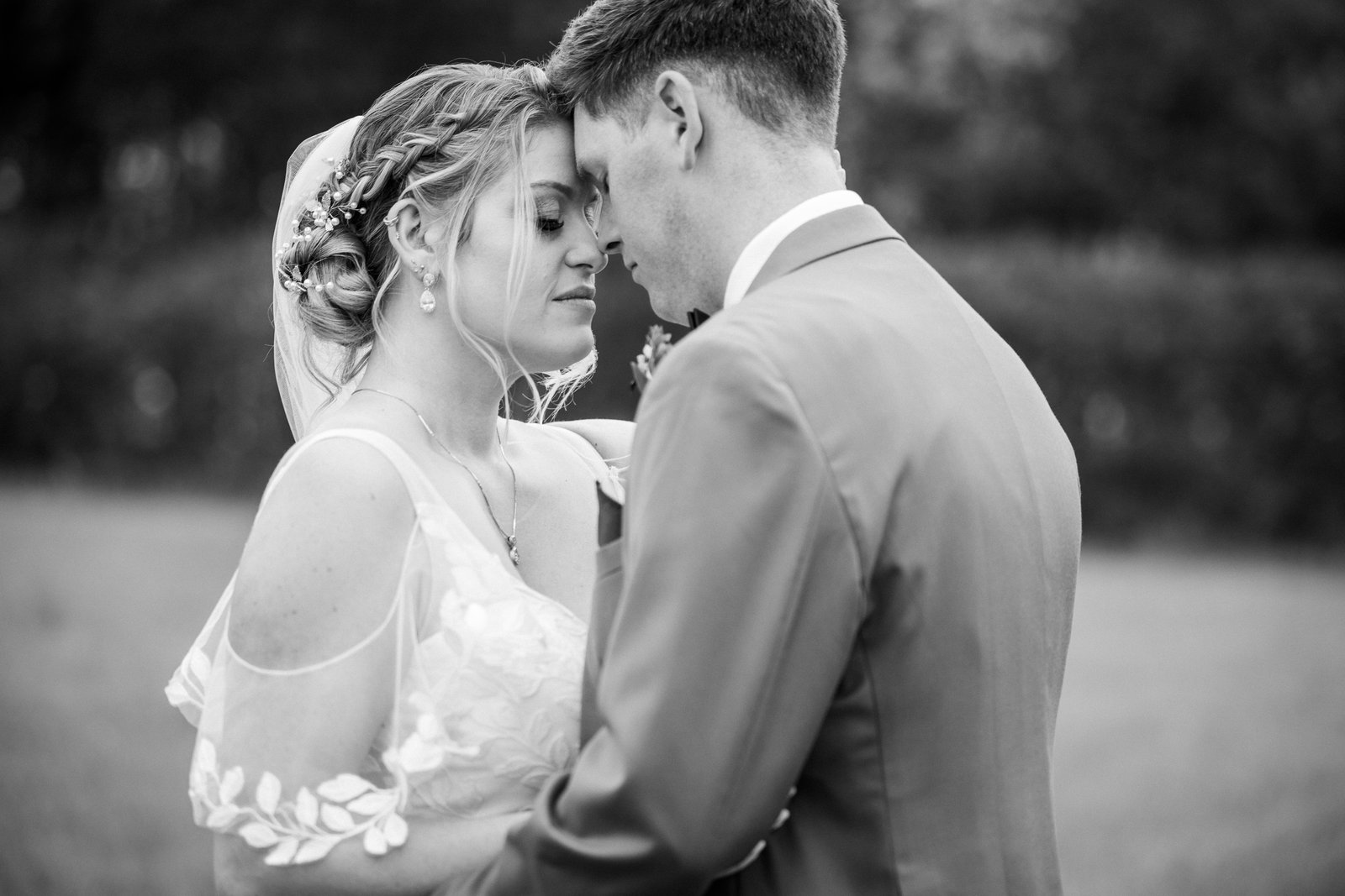 Black and white portrait of the couple forehead to forehead in an open field.