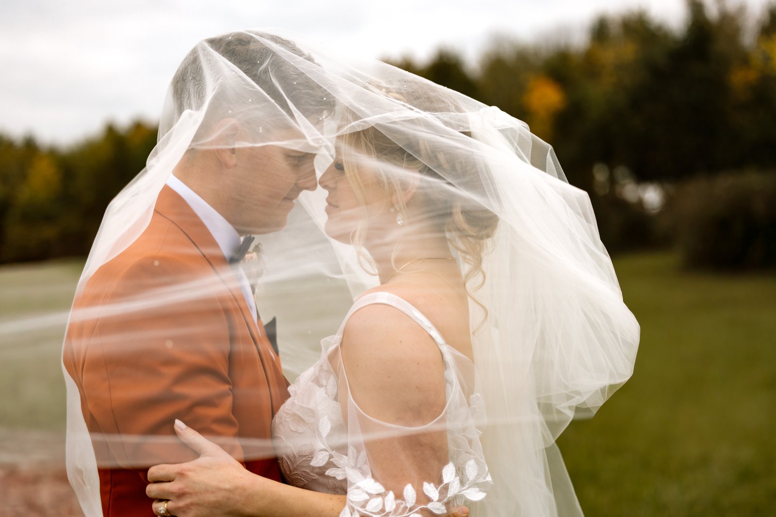The couple standing under the bride's veil with autumn trees behind them.