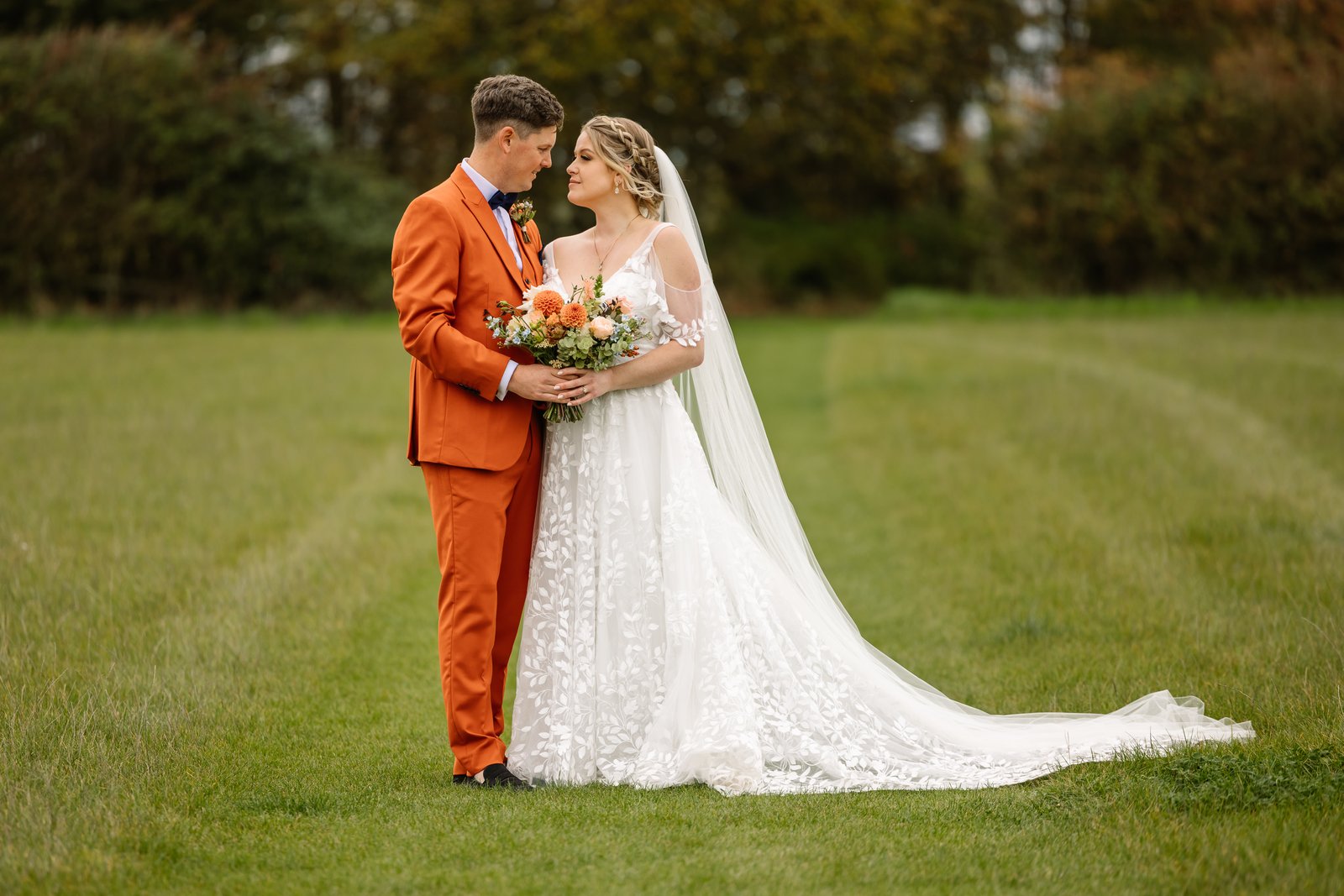 The couple standing together on the grass, the bride's long train laid out behind her.