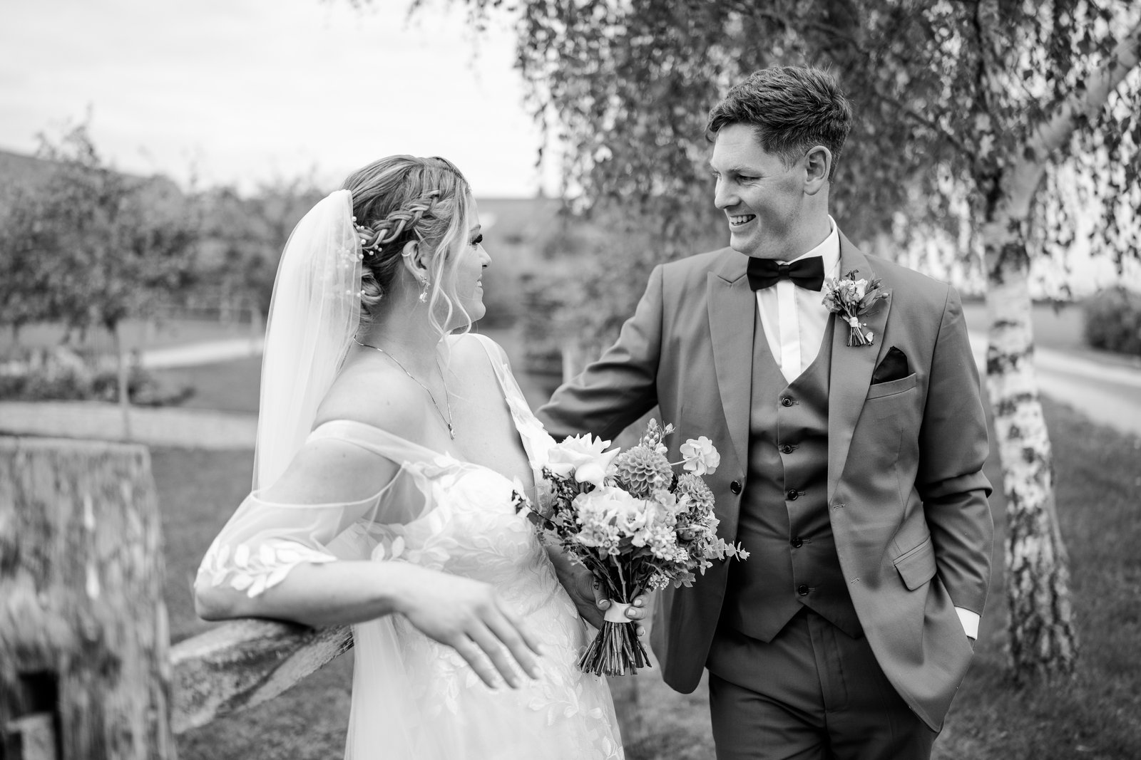 Black and white portrait of the couple by a wooden rail in the venue's gardens.