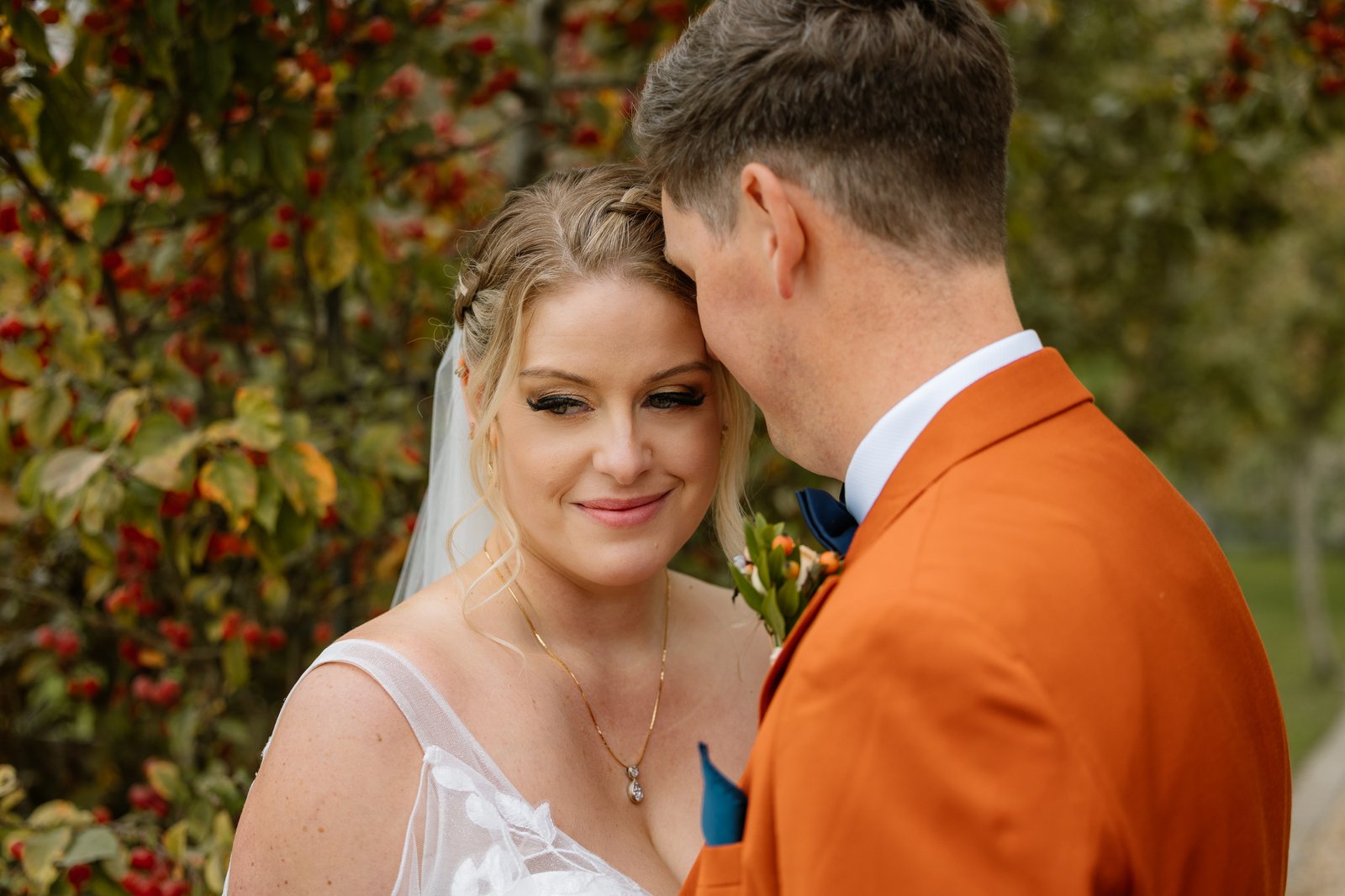 The bride and groom close together beside a tree hung with red berries.