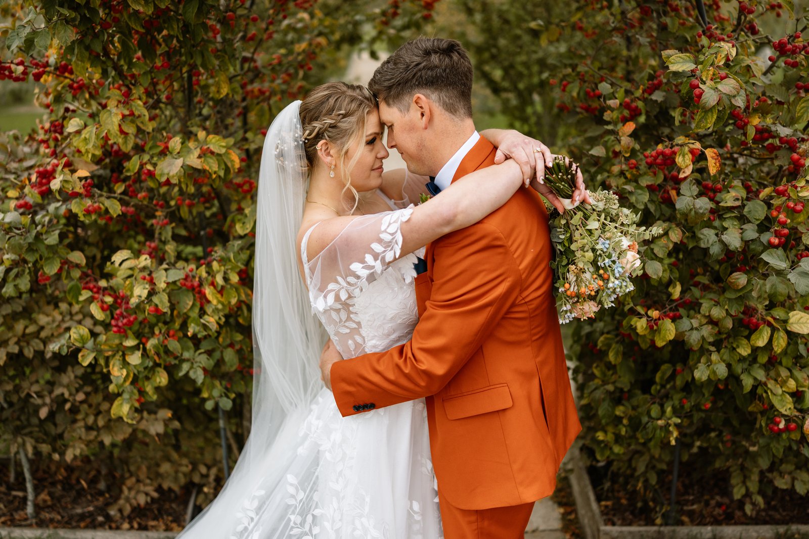 The couple embracing under a berry laden tree in the gardens at Stratton Court Barn.