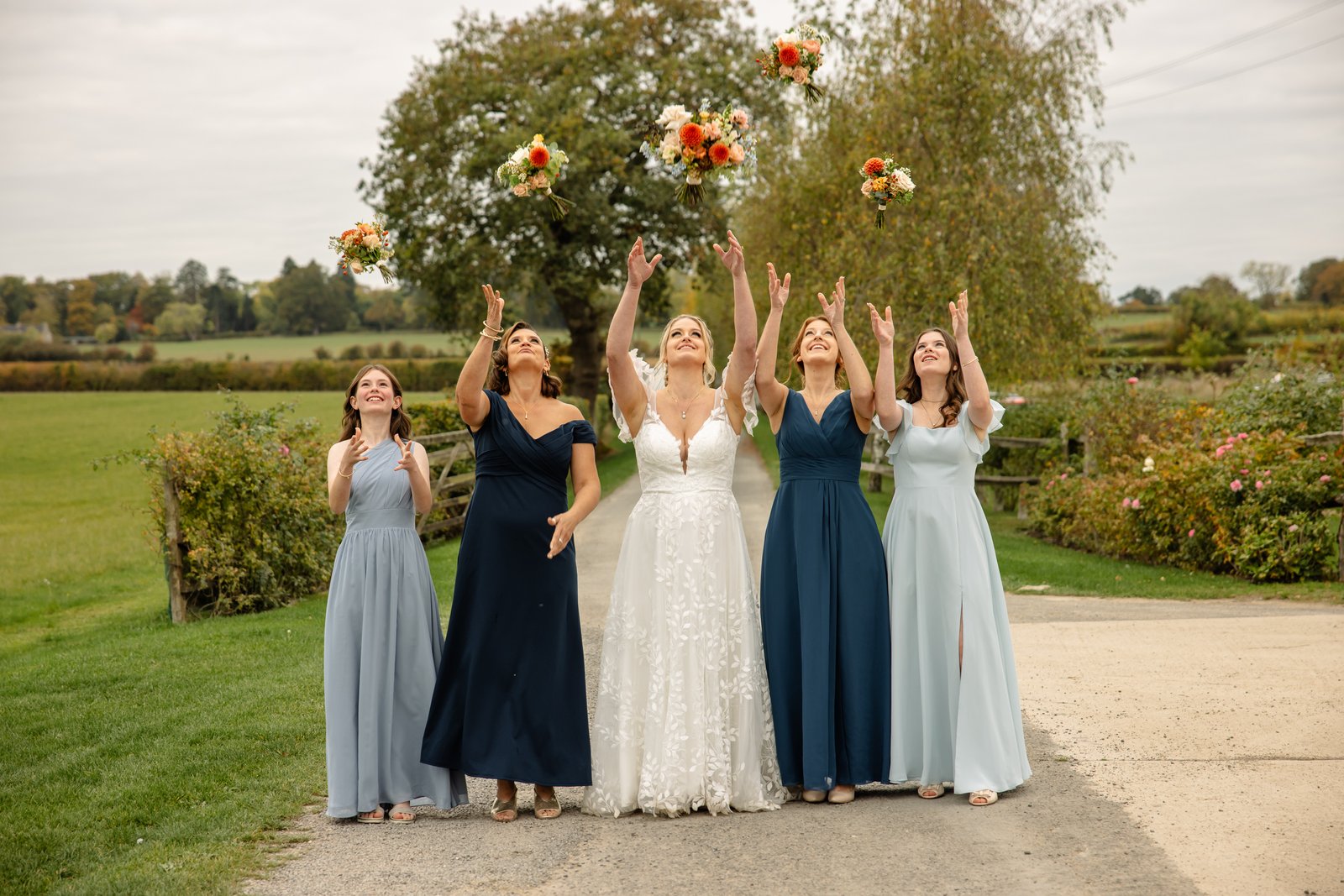 The bridesmaids throwing their bouquets into the air on the path at Stratton Court Barn.