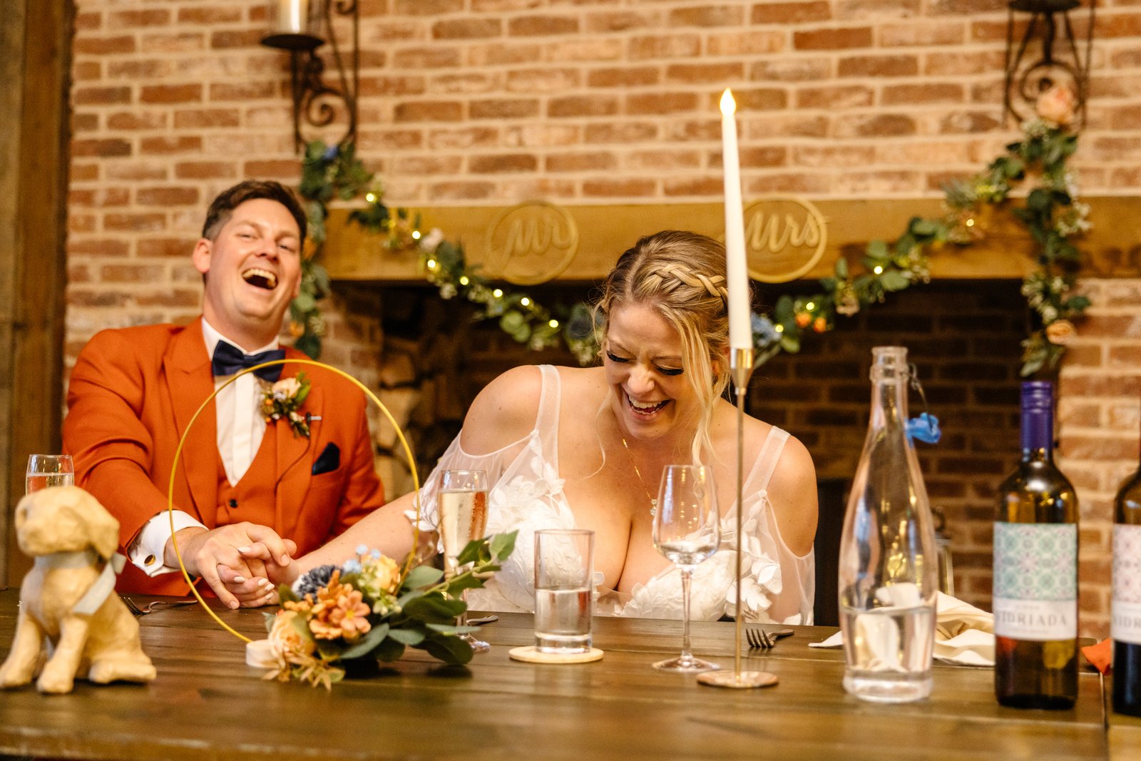 The couple laughing at the top table in front of the brick fireplace at Stratton Court Barn.