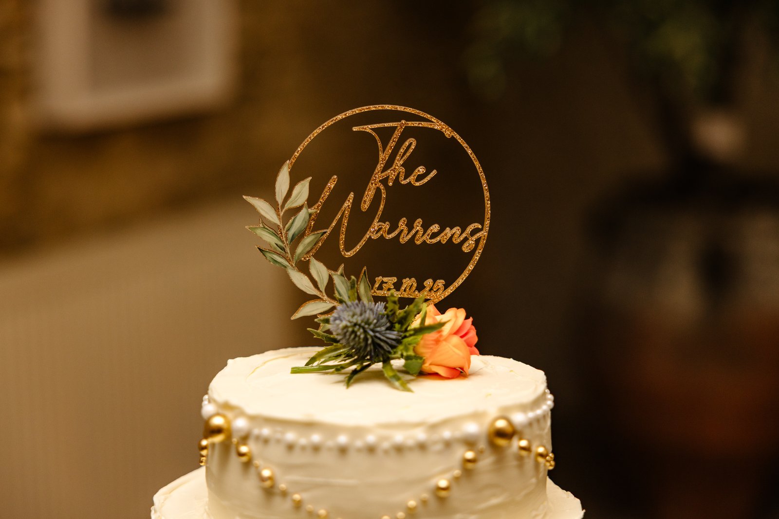 A tiered white wedding cake with a wooden cut out topper and a spray of orange flowers.