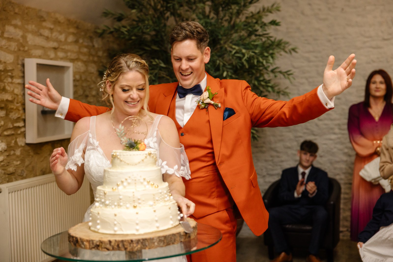 The bride and groom cutting their cake, the groom throwing his arms wide.