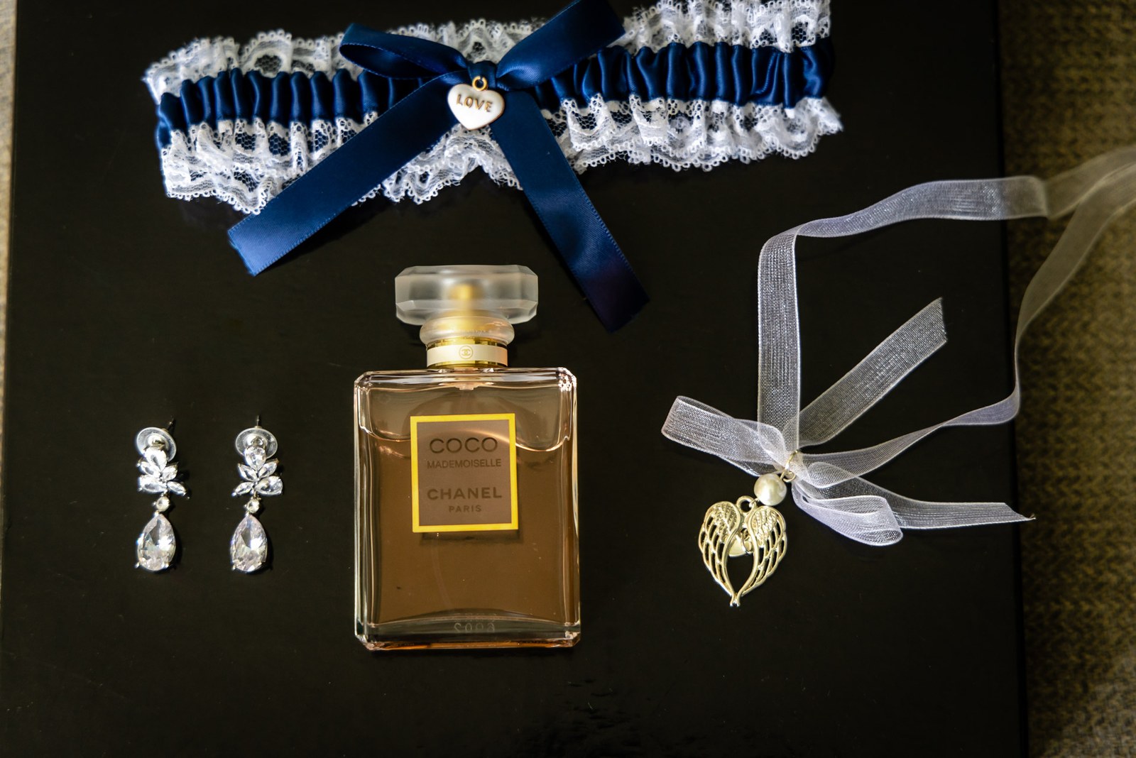 Flat-lay of bridal accessories - a garter with a navy bow, drop earrings and perfume