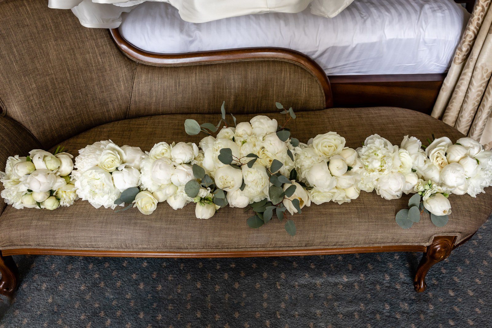 White roses and eucalyptus arranged along an antique wooden chaise