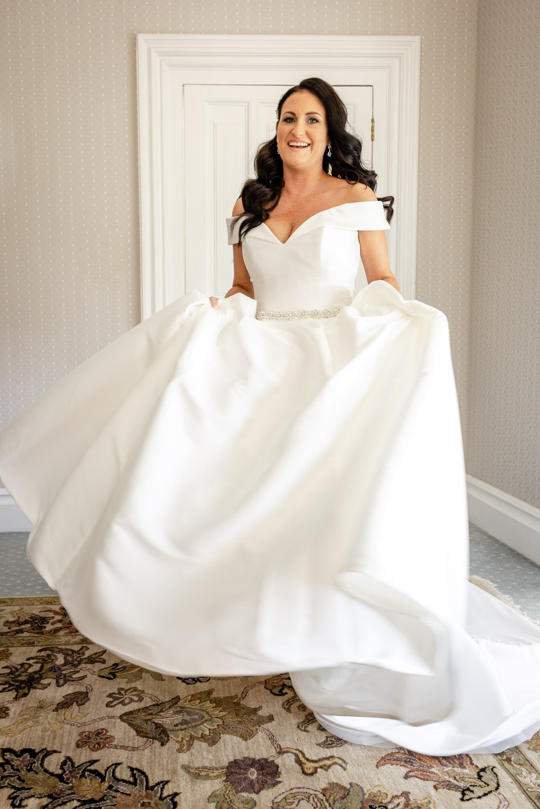 Bride holding out the full skirt of her off-shoulder satin gown