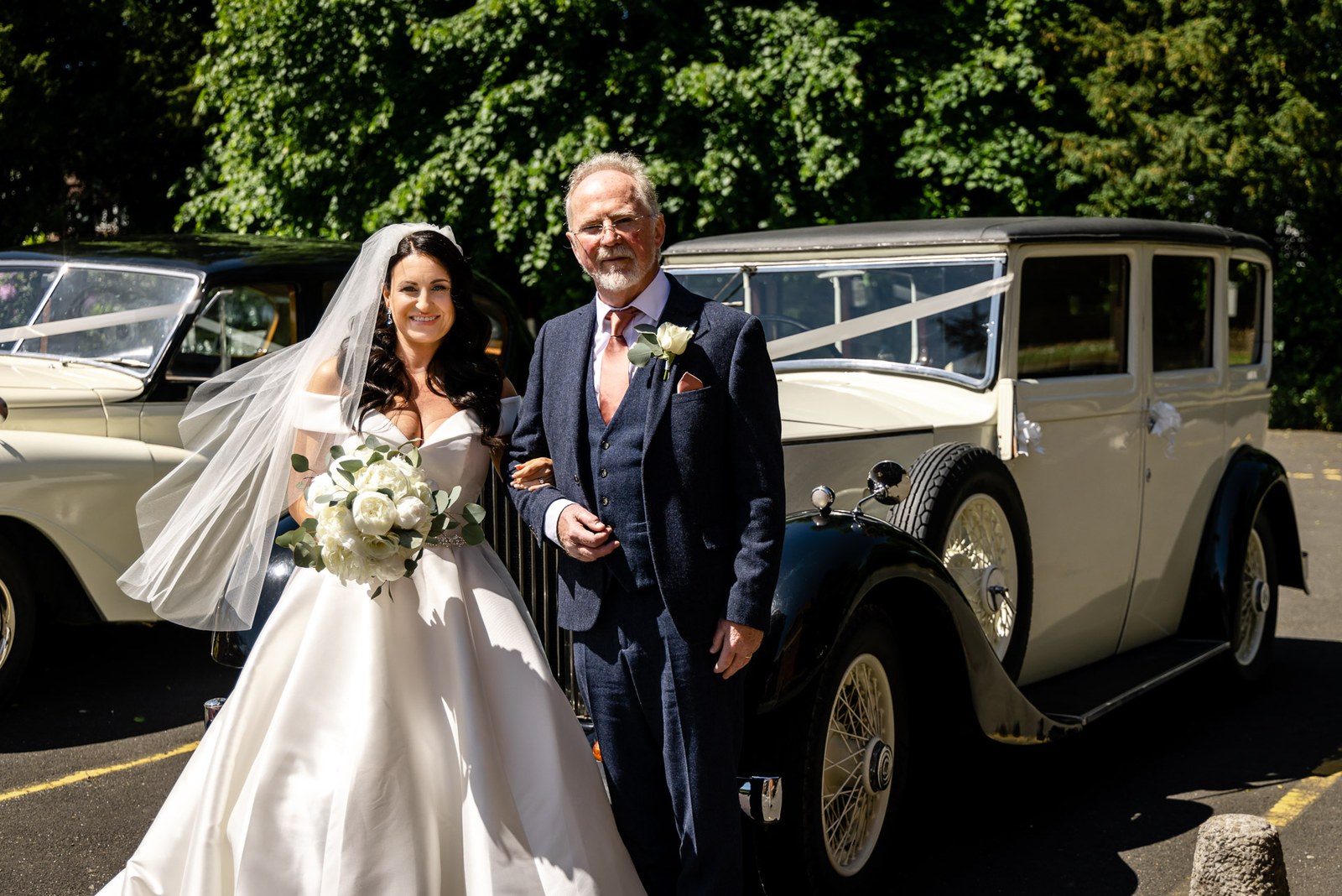 Bride on her father's arm beside a vintage car outside the church