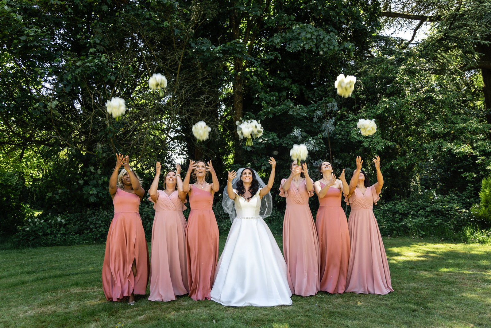 Bride and bridesmaids tossing their bouquets into the air beneath a tree