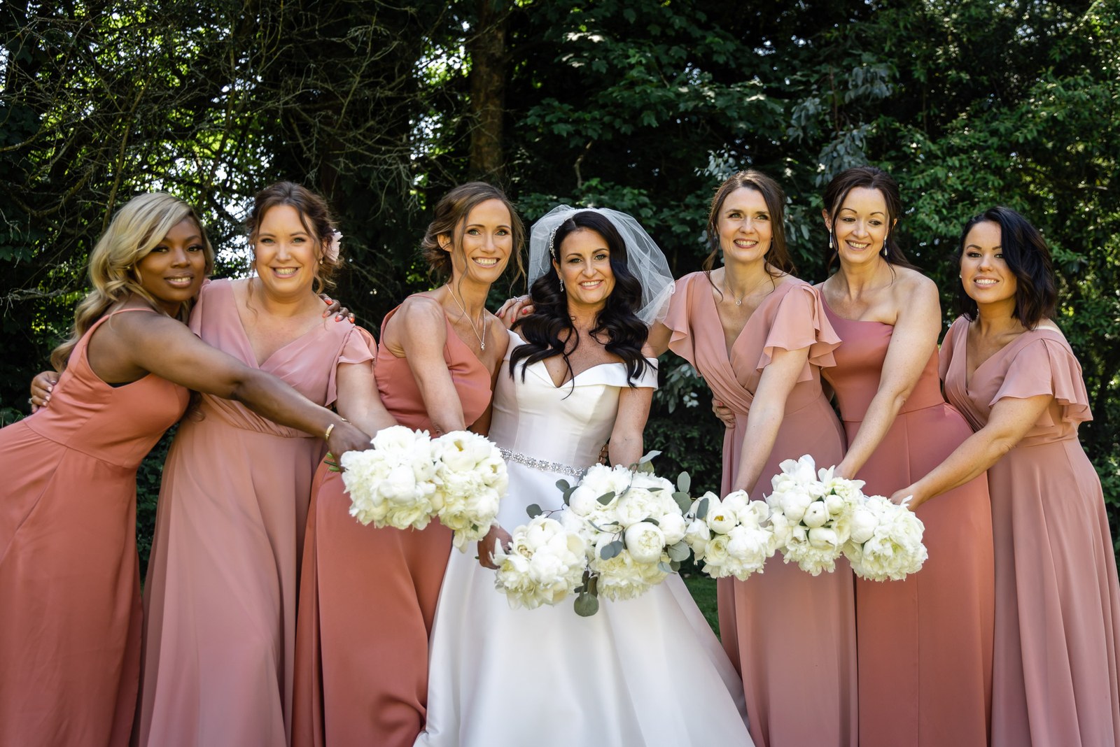 Bride with her bridesmaids in rust gowns holding white bouquets