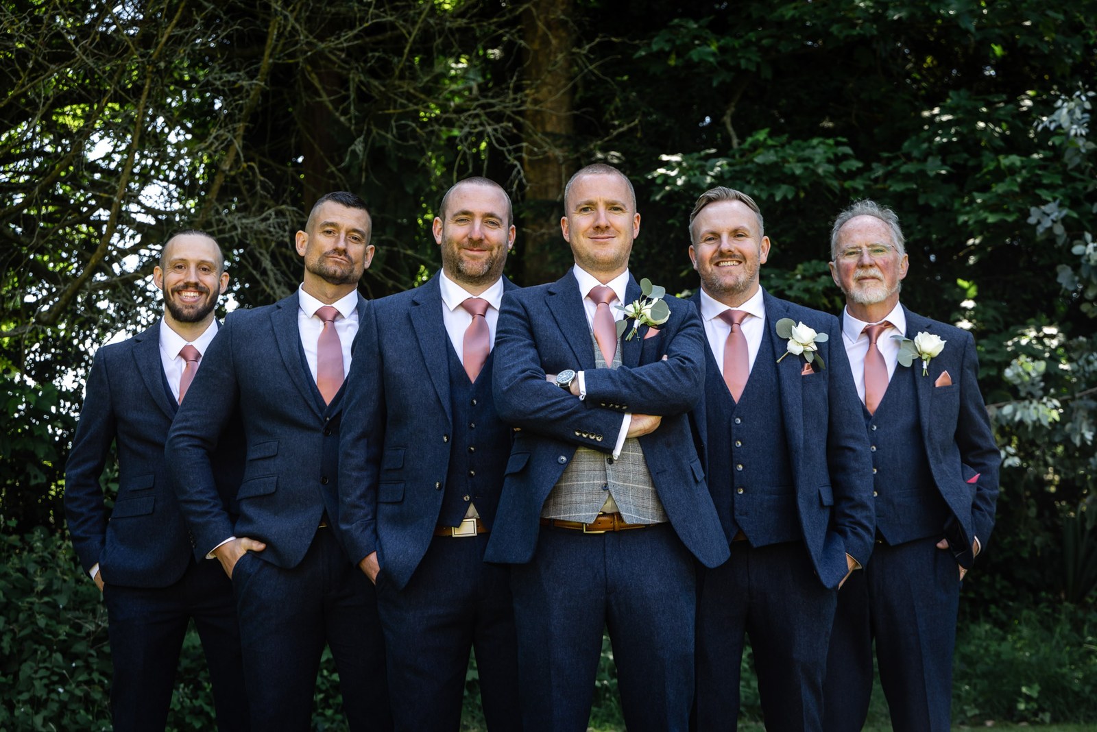 The groom with his groomsmen in navy three-piece suits outdoors