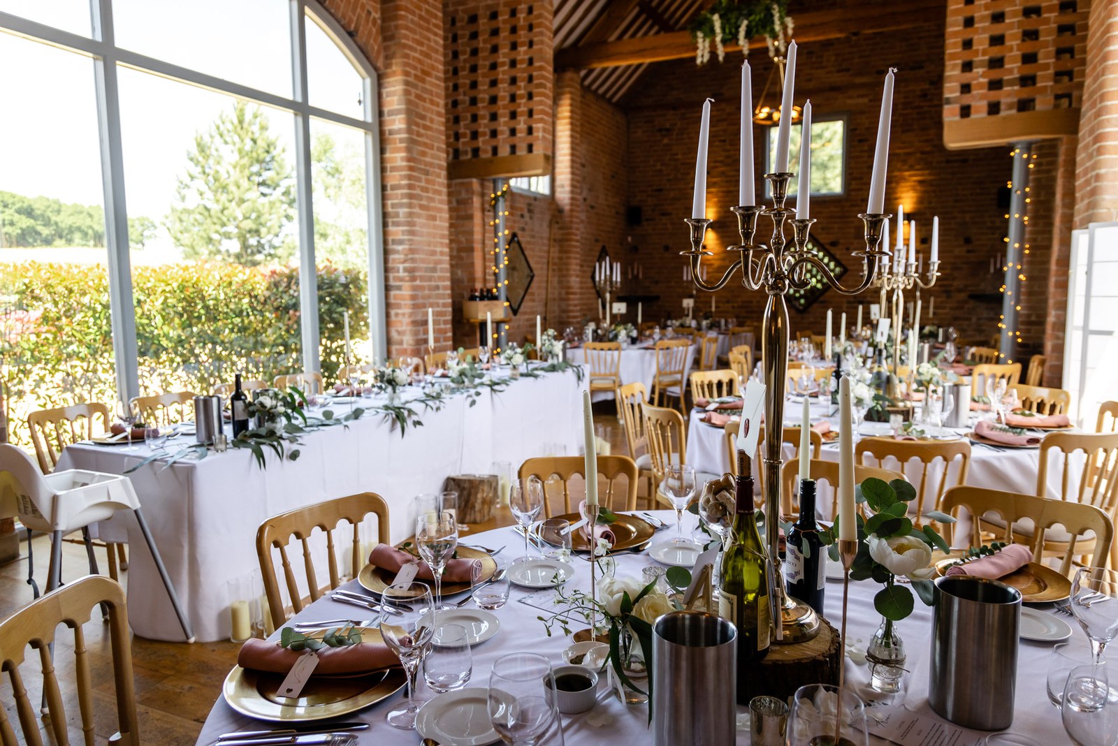 The reception table set with silver candelabra beneath brick walls at Swallows Nest Barn
