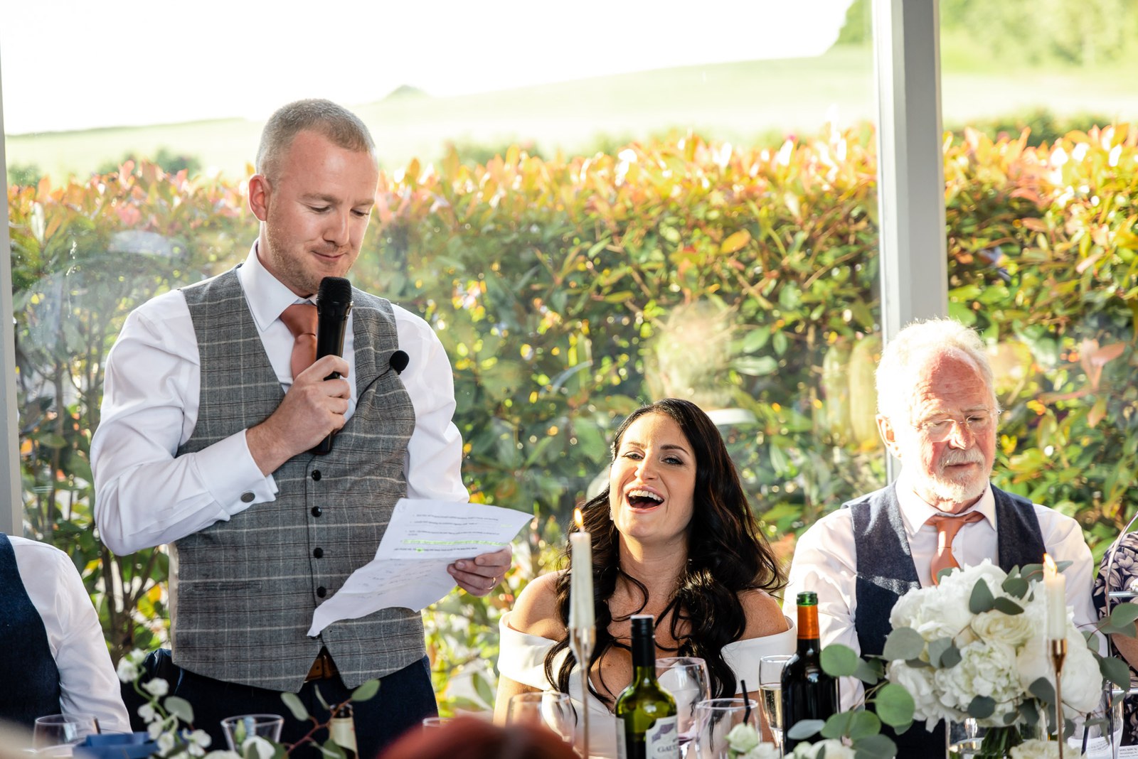 The groom giving a speech as the bride laughs at the top table