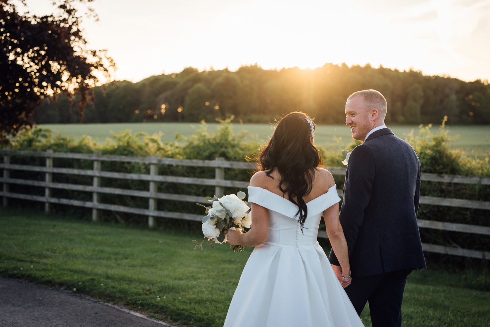 Bride and groom facing each other in the fields beside Swallows Nest Barn at sunset