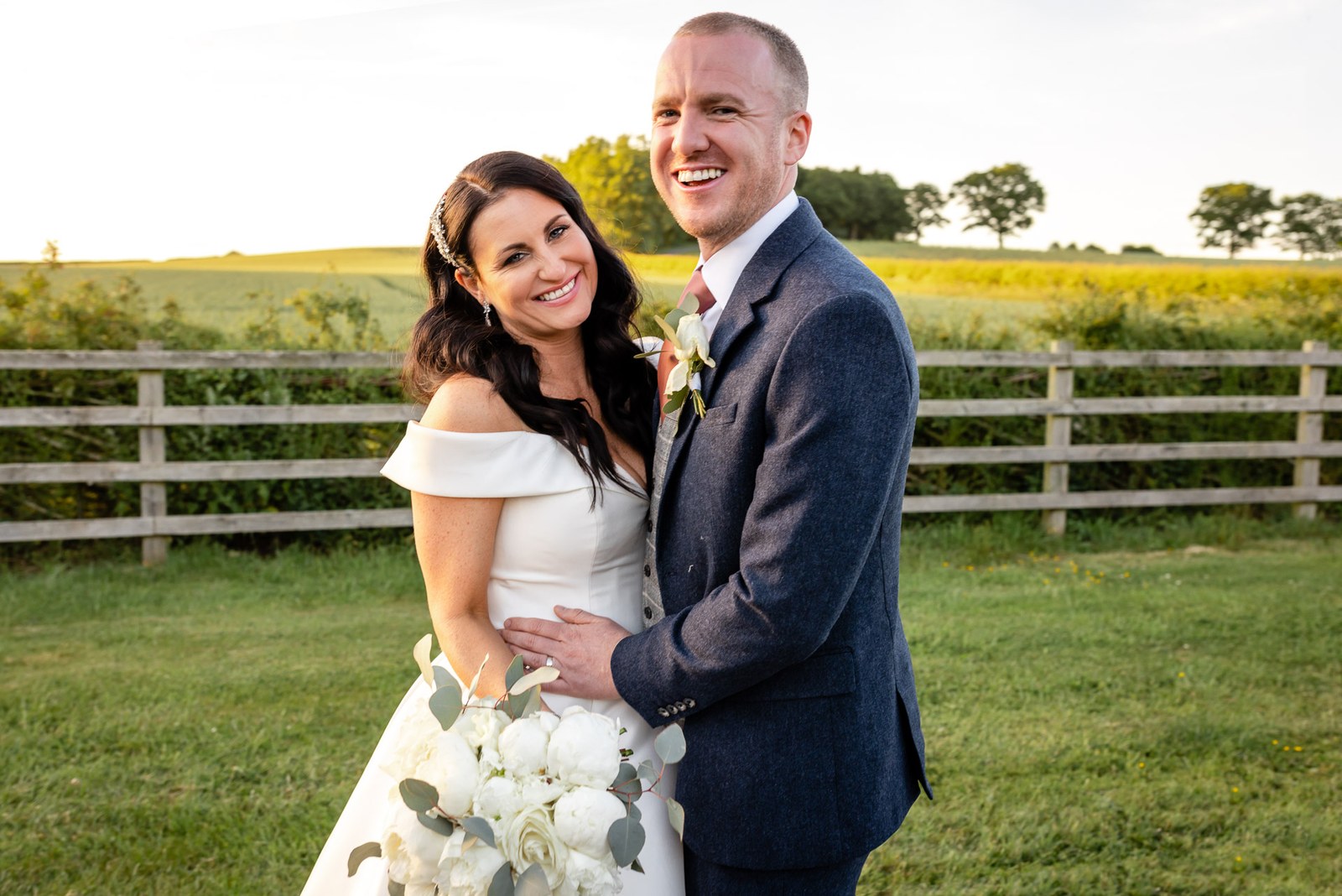 The couple embracing beside a golden field at sunset