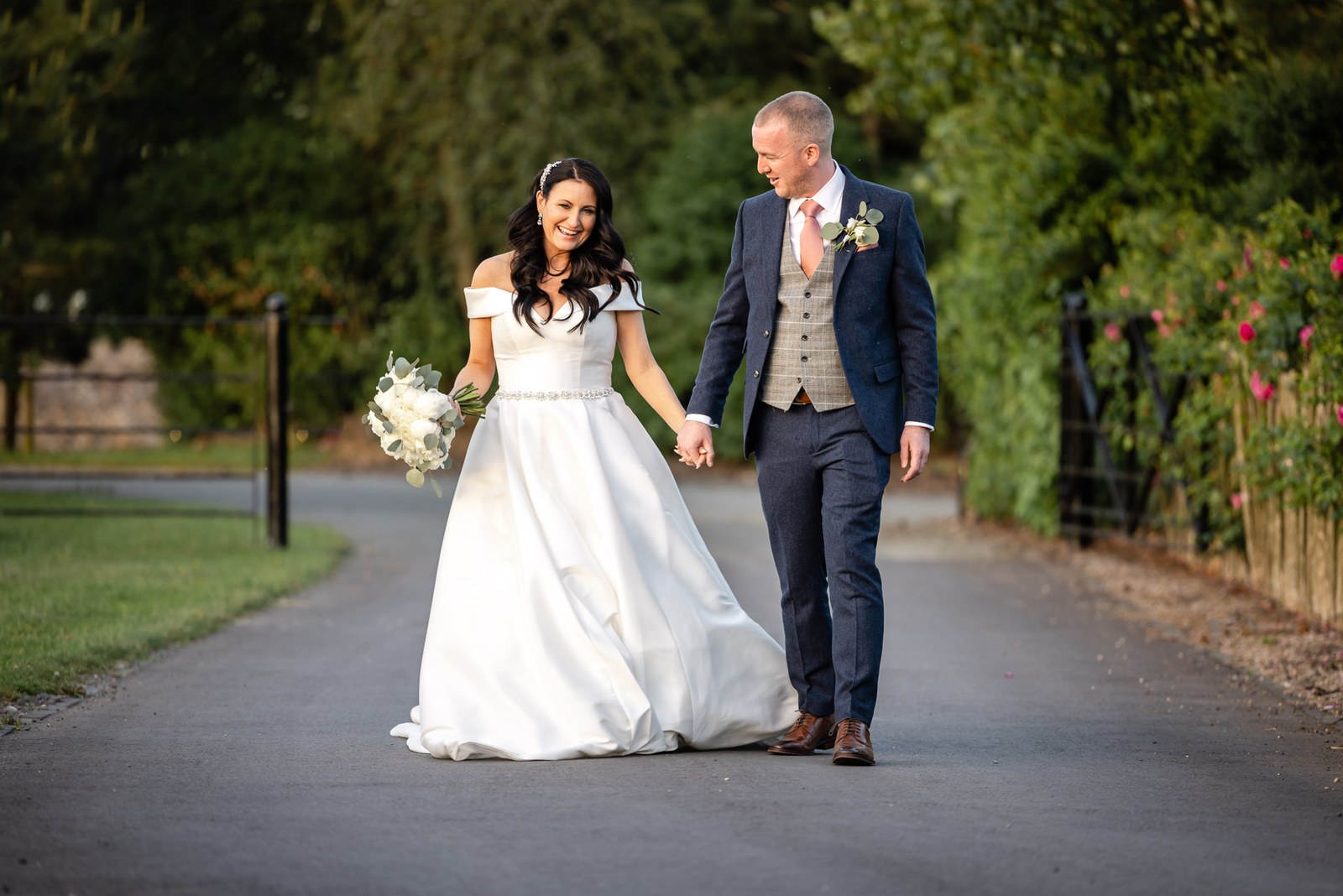 Newlyweds walking hand in hand down a lane at dusk
