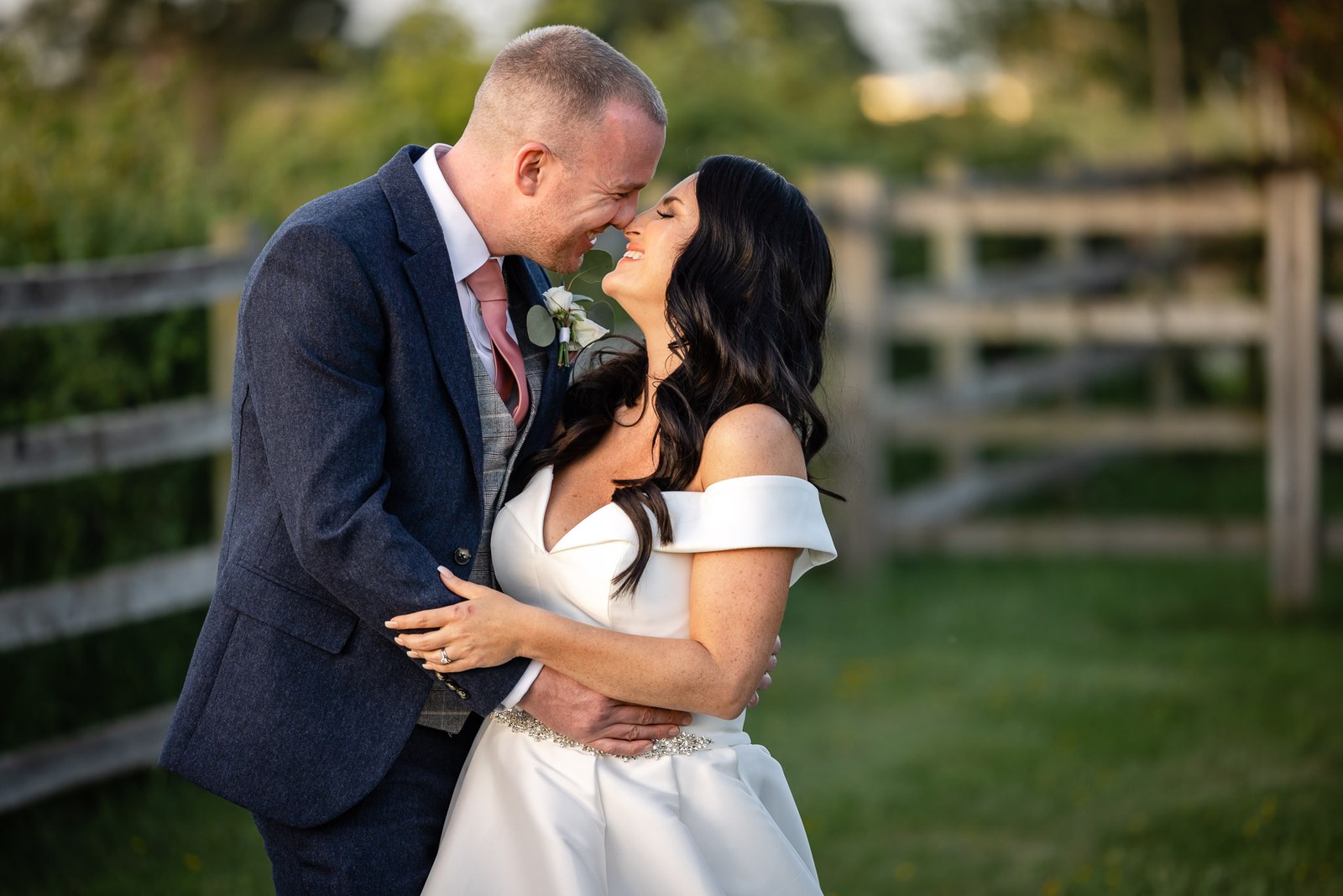 Bride and groom embracing by a wooden gate in the fields at golden hour