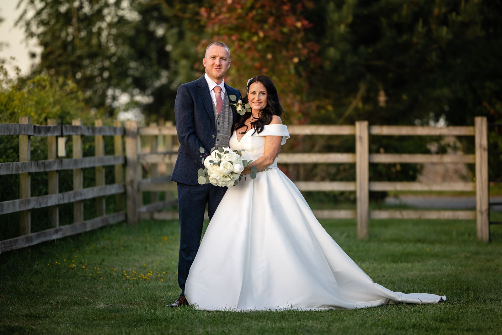 Bride and groom by a post-and-rail fence in the fields beside Swallows Nest Barn
